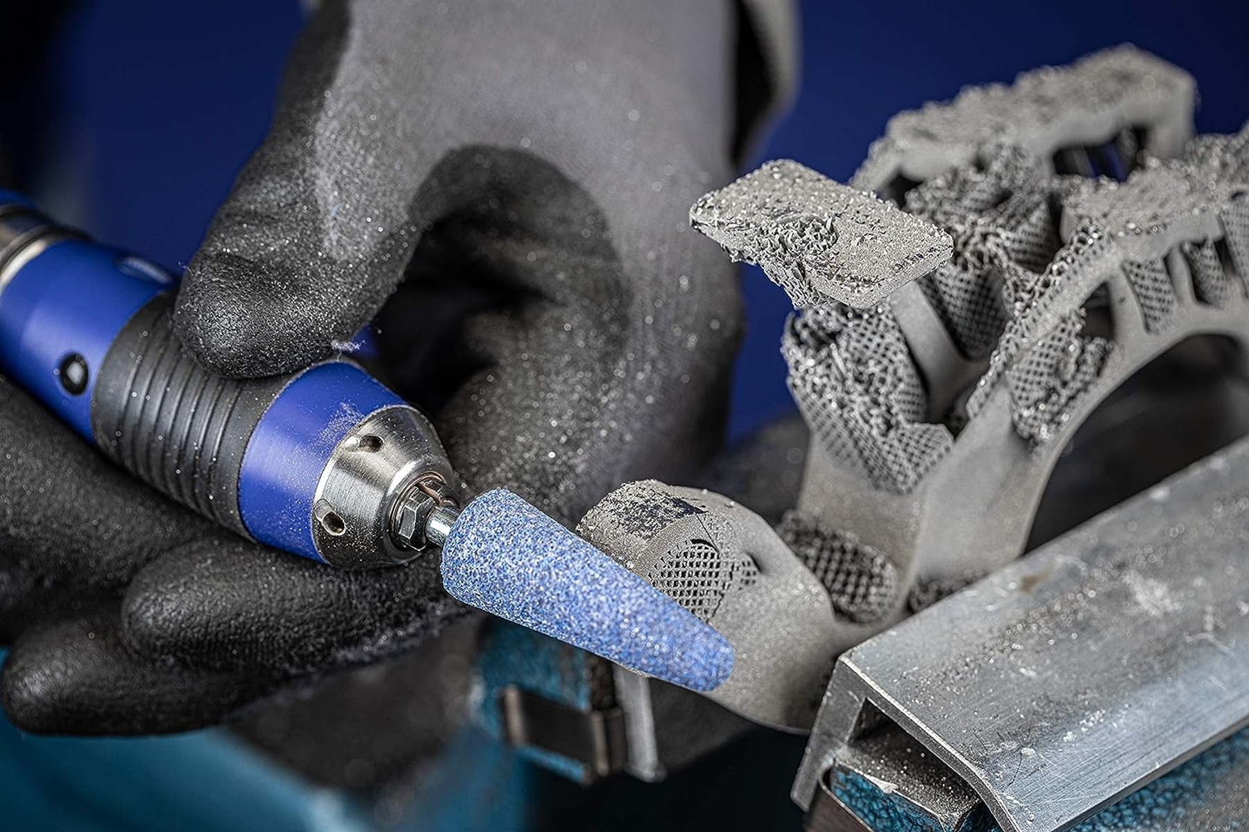 Person bearbeitet mit blau-schwarzem Werkzeug Metallteil mit komplexem Design.
