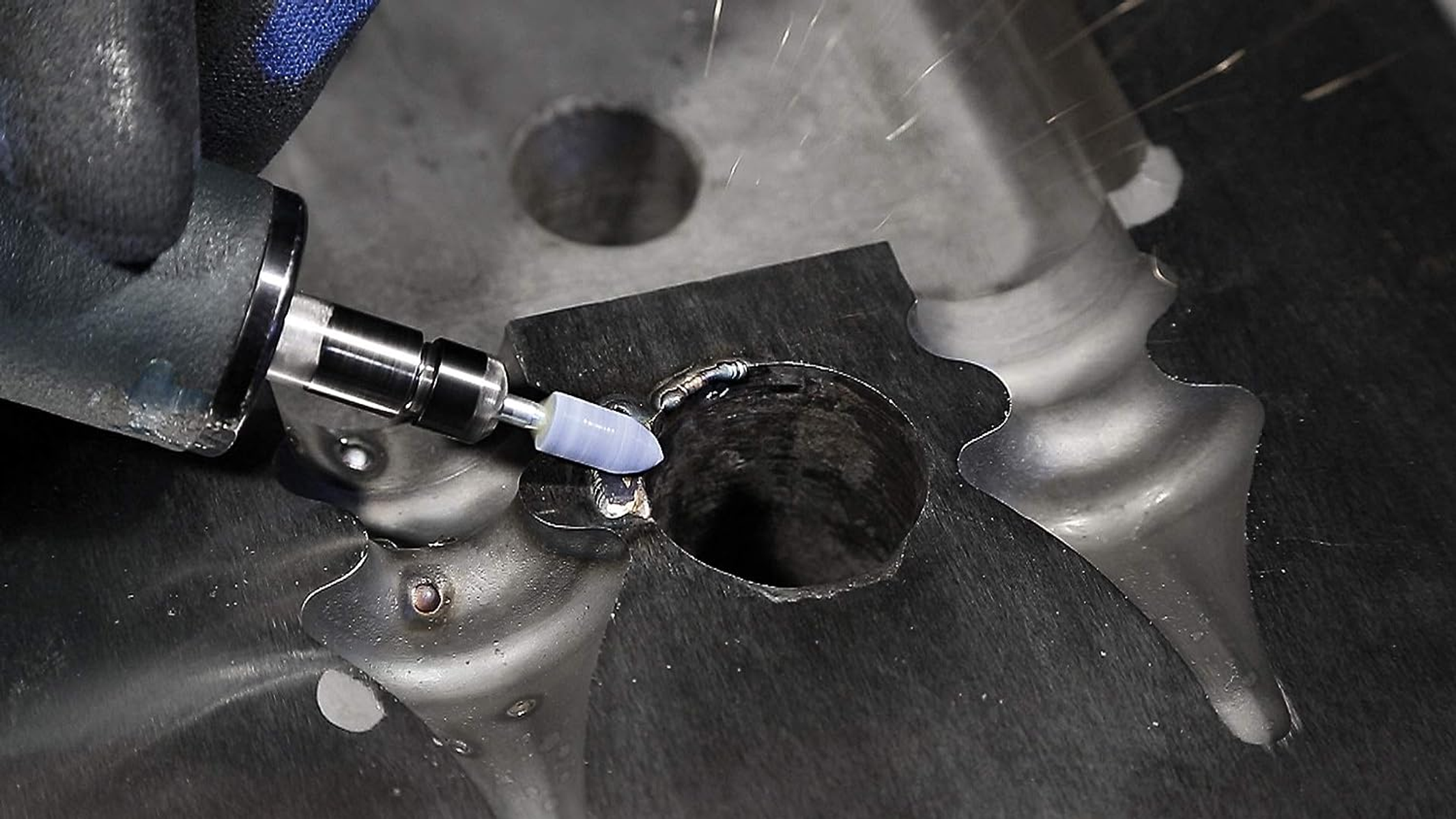 Nahaufnahme eines Werkzeugs, das eine Metalloberfläche schleift. Funken fliegen, während das Werkzeug Material abträgt.