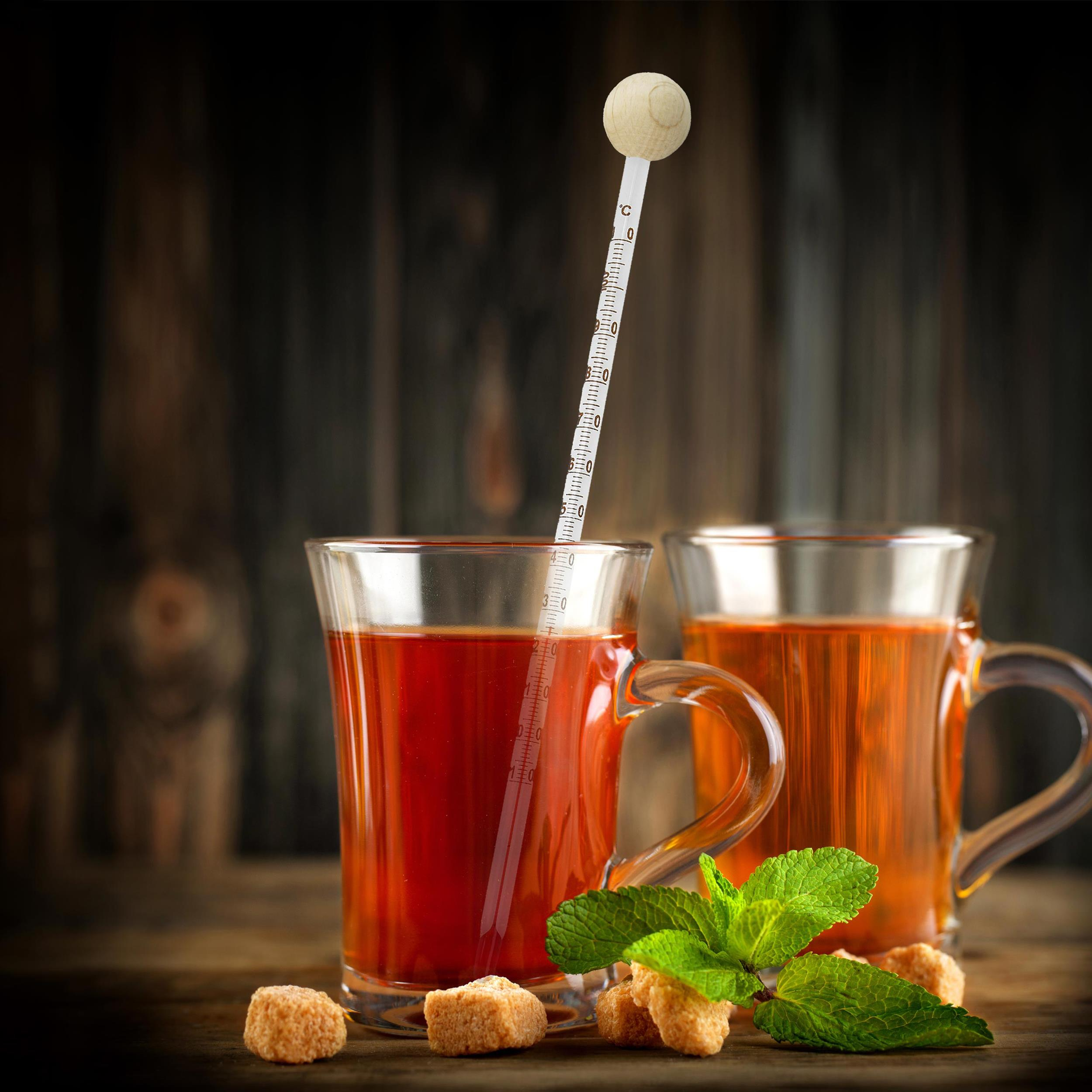 Zwei Tassen Tee mit Thermometer, Minze und Würfelzucker auf Holzoberfläche.