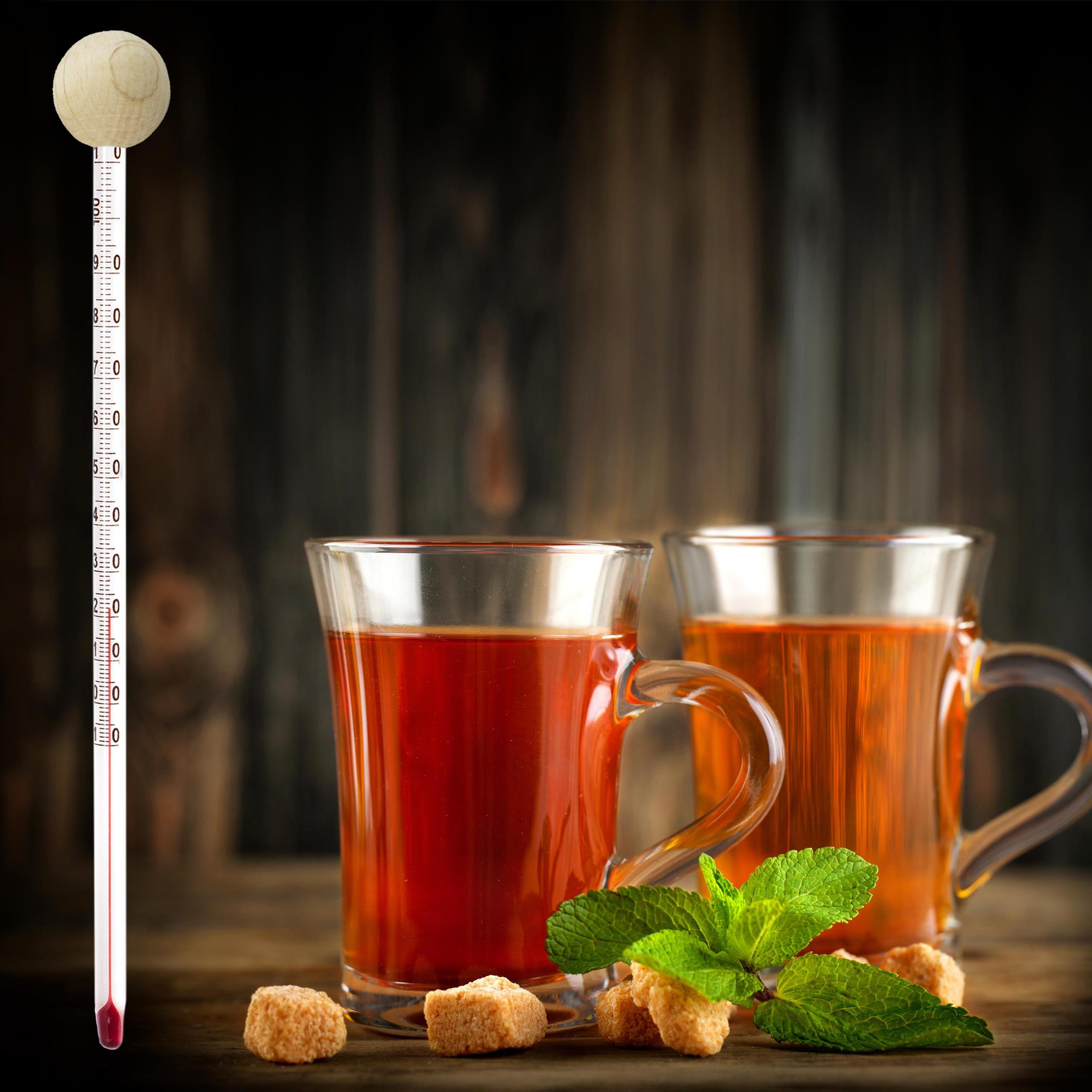 Zwei Gläser Tee, Zuckerwürfel, Minzblätter und ein Thermometer auf einem Holztisch.