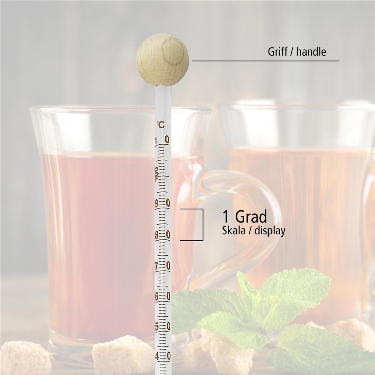 Ein Glasthermometer in einem Glas Tee, mit Beschriftungen für Griff, Anzeige und Temperaturskala.