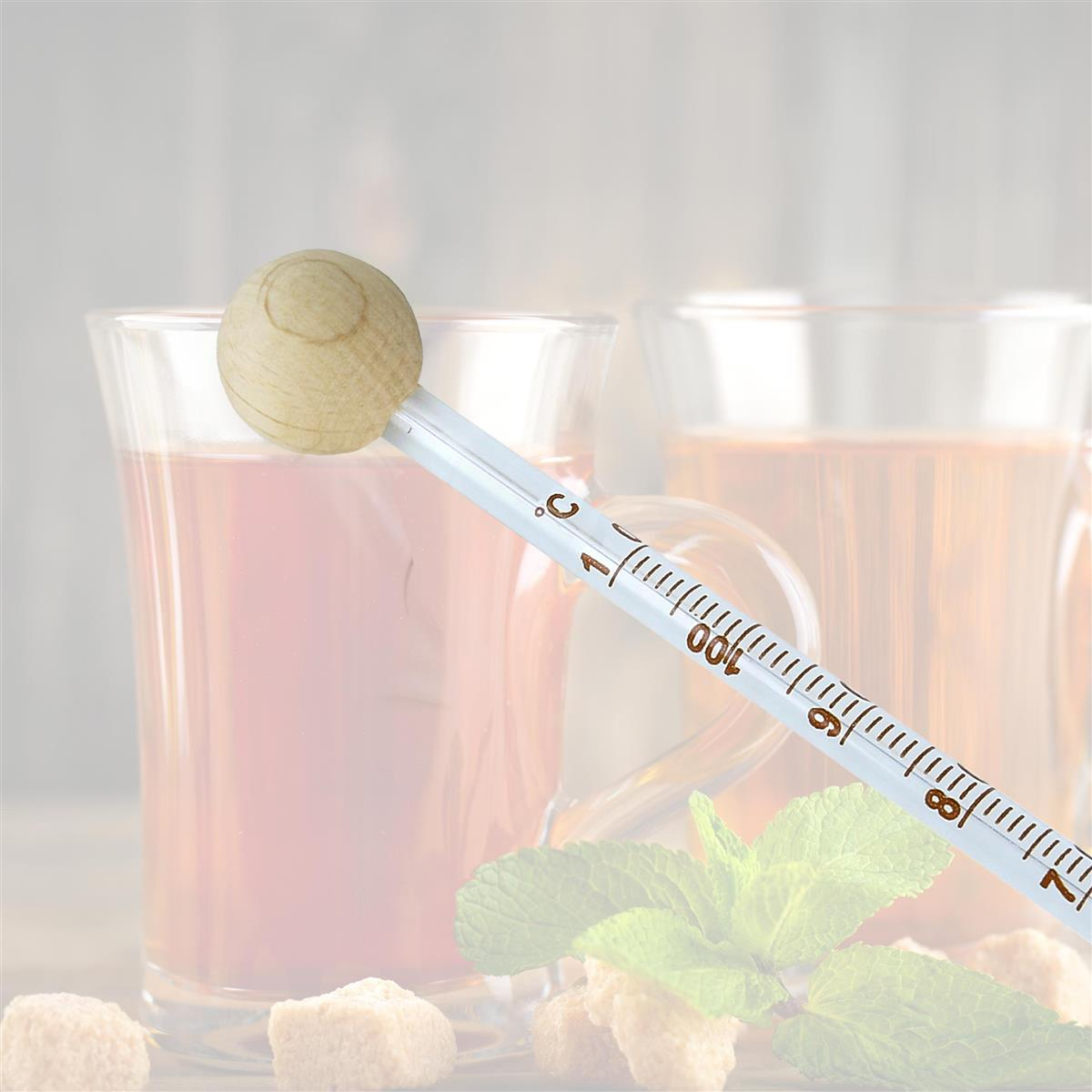 Teetasse mit Holzthermometer, Minze und Würfelzucker, unscharfer Hintergrund.