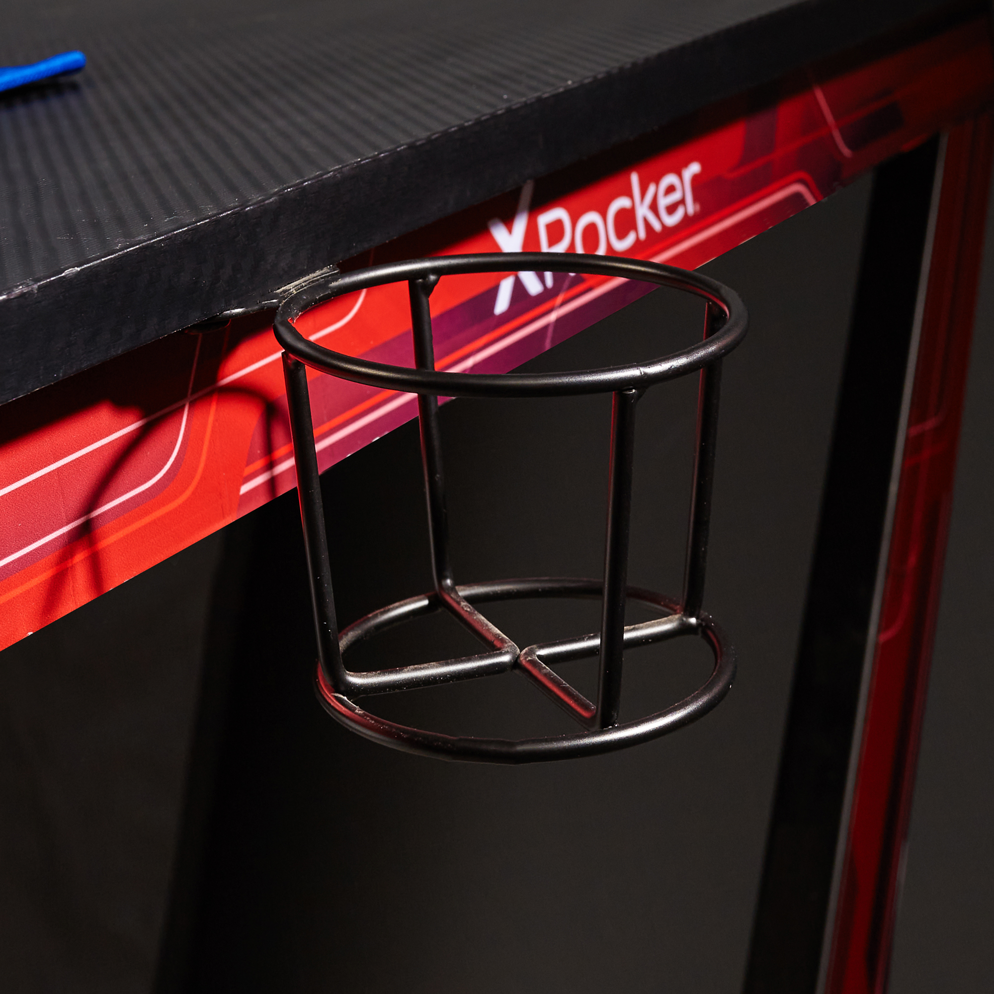 Ein schwarzer Getränkehalter an einem rot-schwarzen Gaming-Schreibtisch befestigt. Das X Rocker-Logo ist sichtbar.