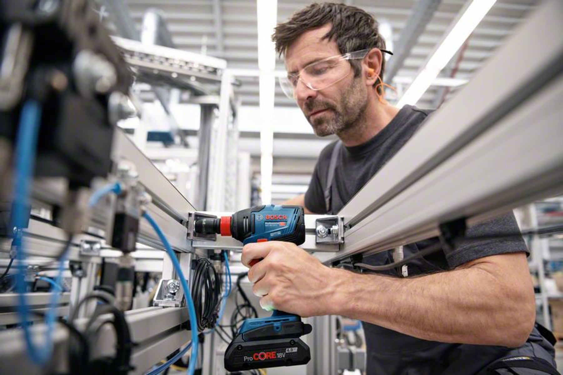 Mann mit Schutzbrille benutzt einen blauen Bosch Akkuschrauber an einer Maschine.