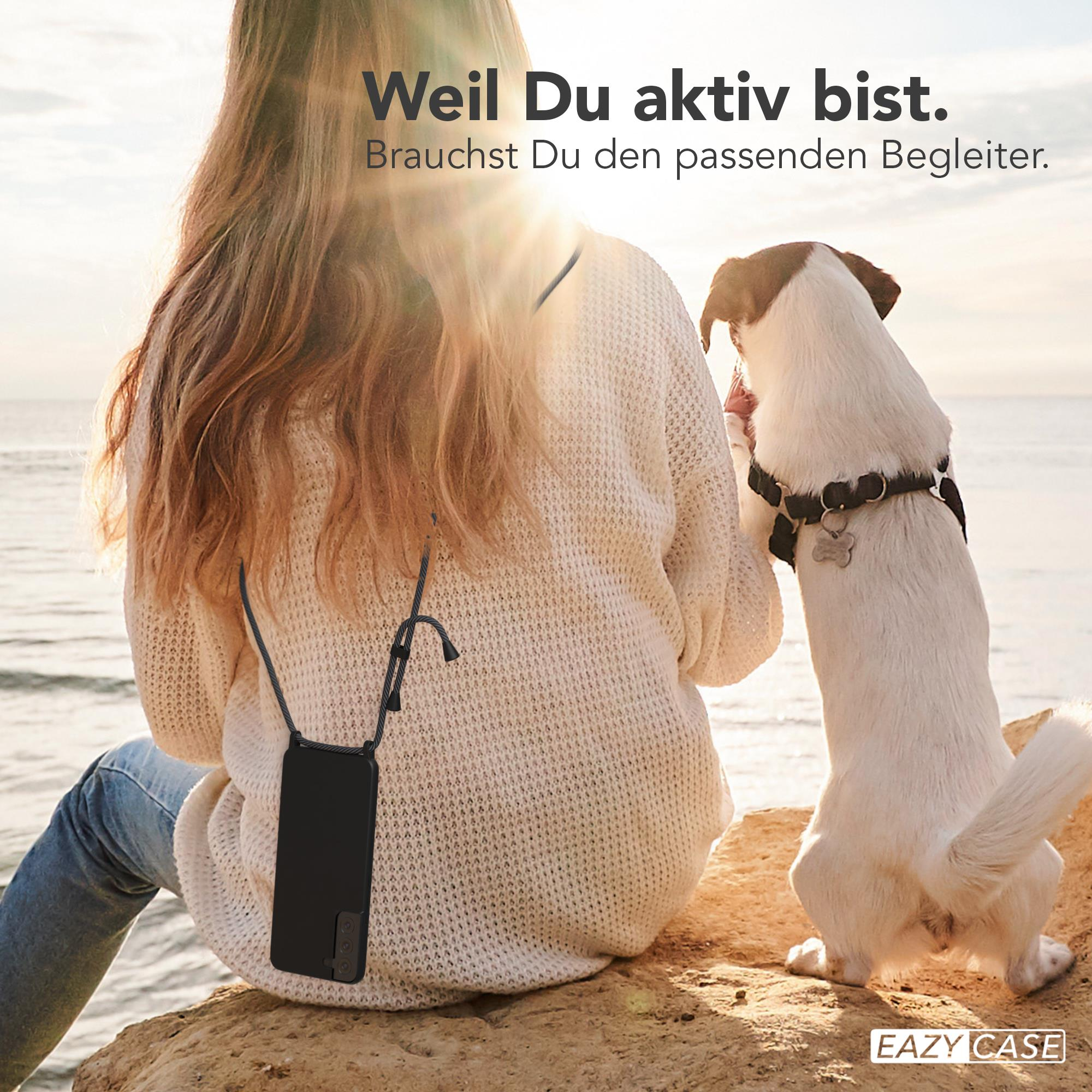 Frau mit langen Haaren sitzt mit einem Hund auf einem Felsen. Eine Handyhülle hängt um ihren Hals.