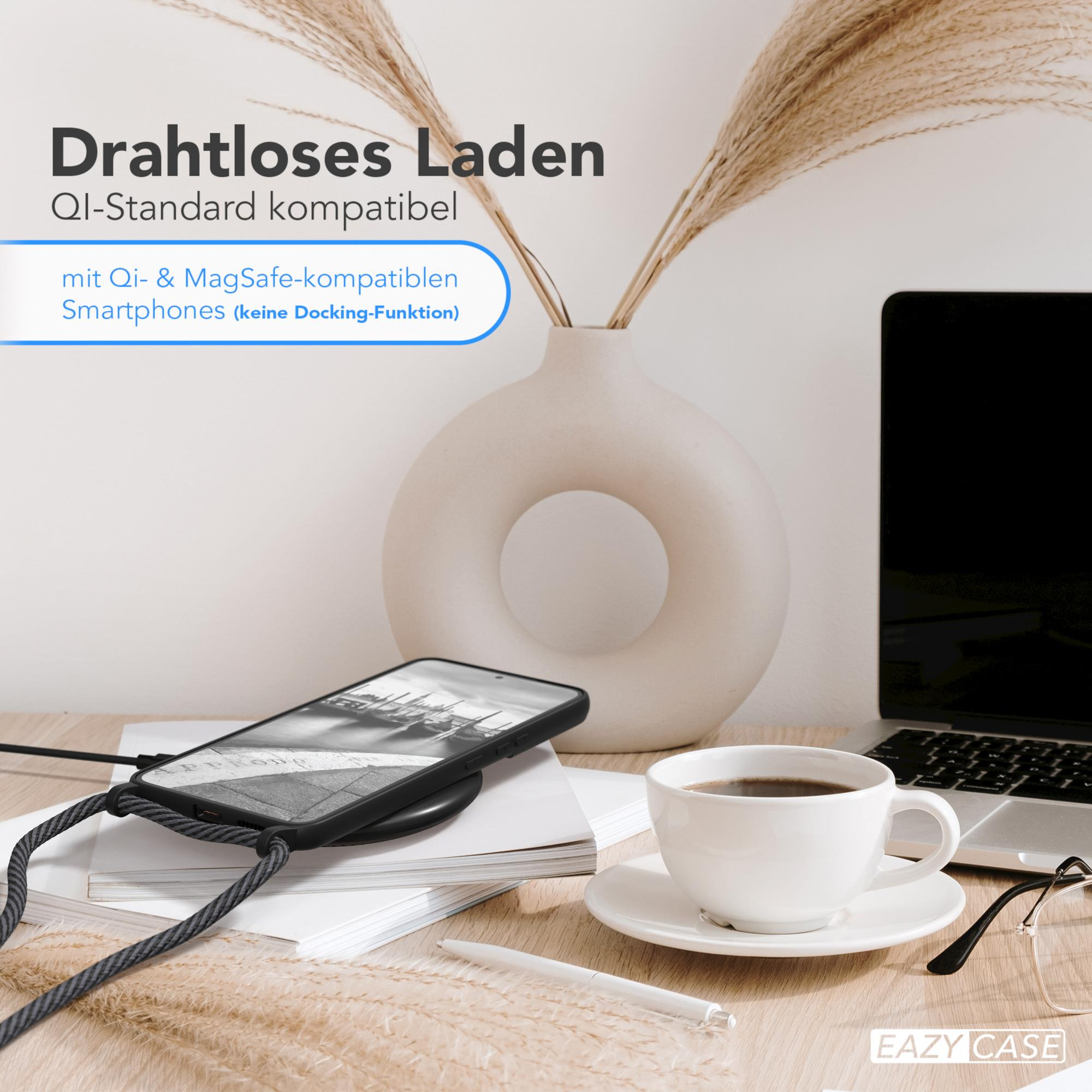 Ein Telefon auf einem kabellosen Ladegerät mit einer Kaffeetasse und einem Laptop im Hintergrund.