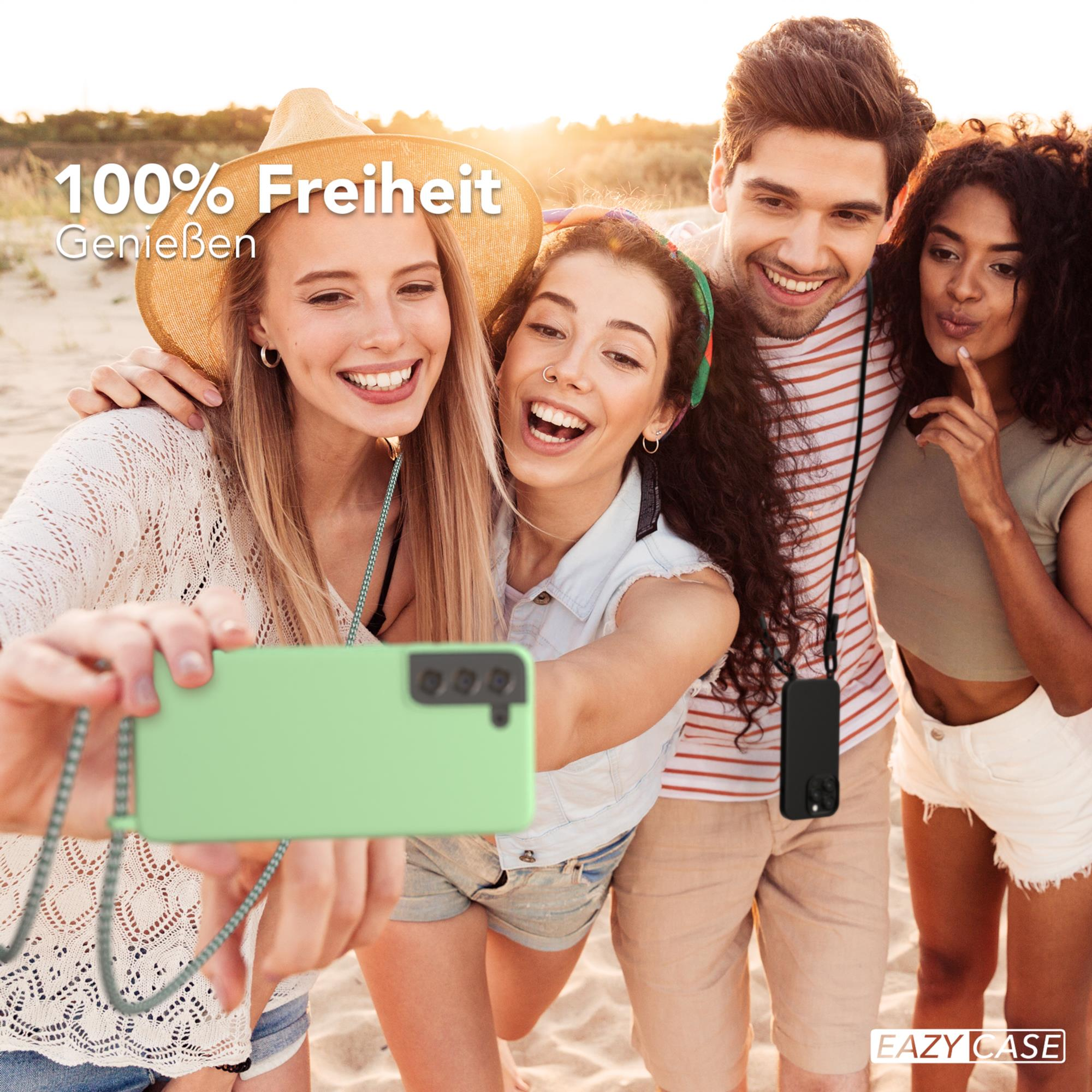 Vier Personen machen Selfie, lächeln. Einer hält mintfarbenes Telefon. Strandhintergrund.