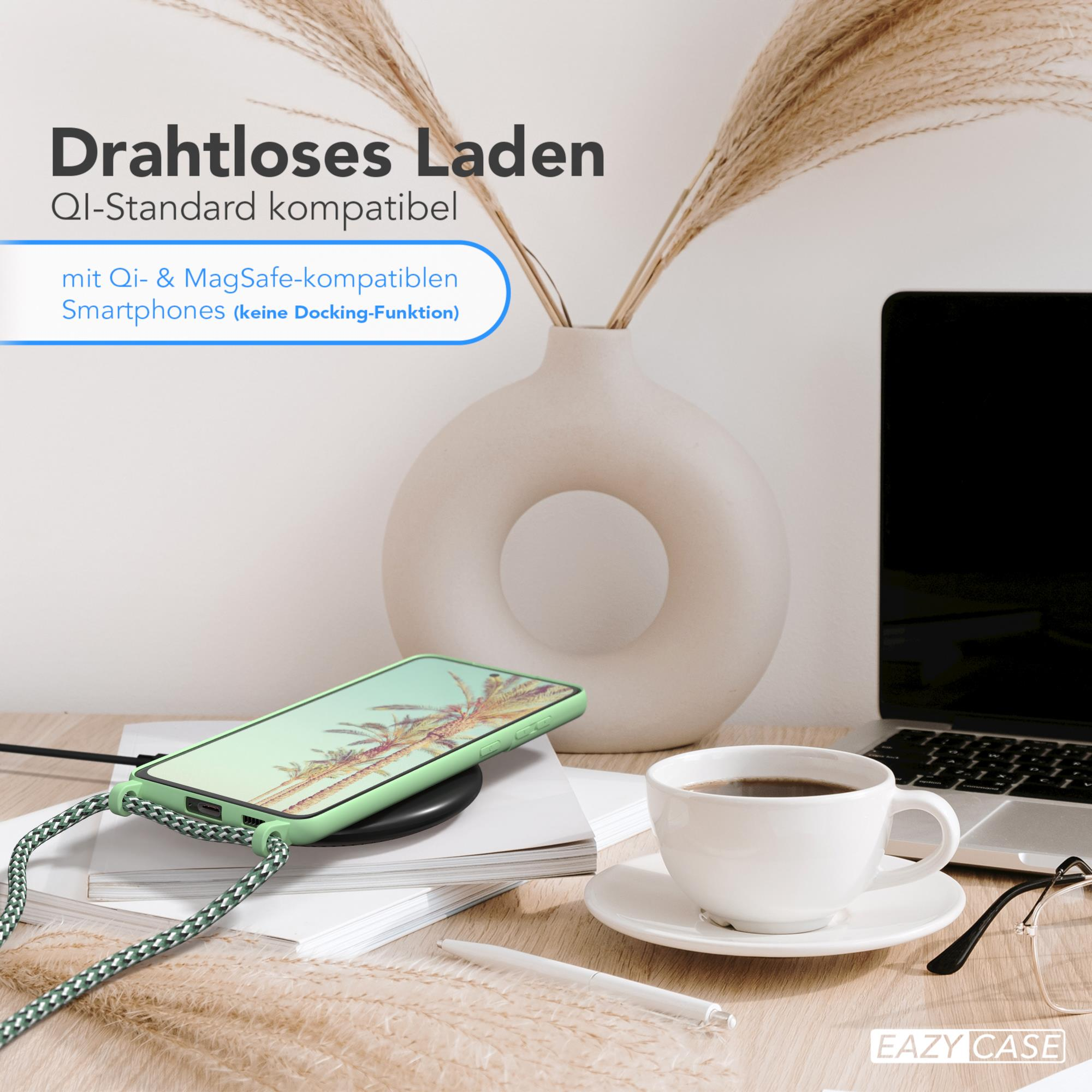 Ein Telefon auf einem kabellosen Ladegerät, neben einer Vase mit Pflanzen, einer Kaffeetasse und einer Brille auf einem Holztisch.