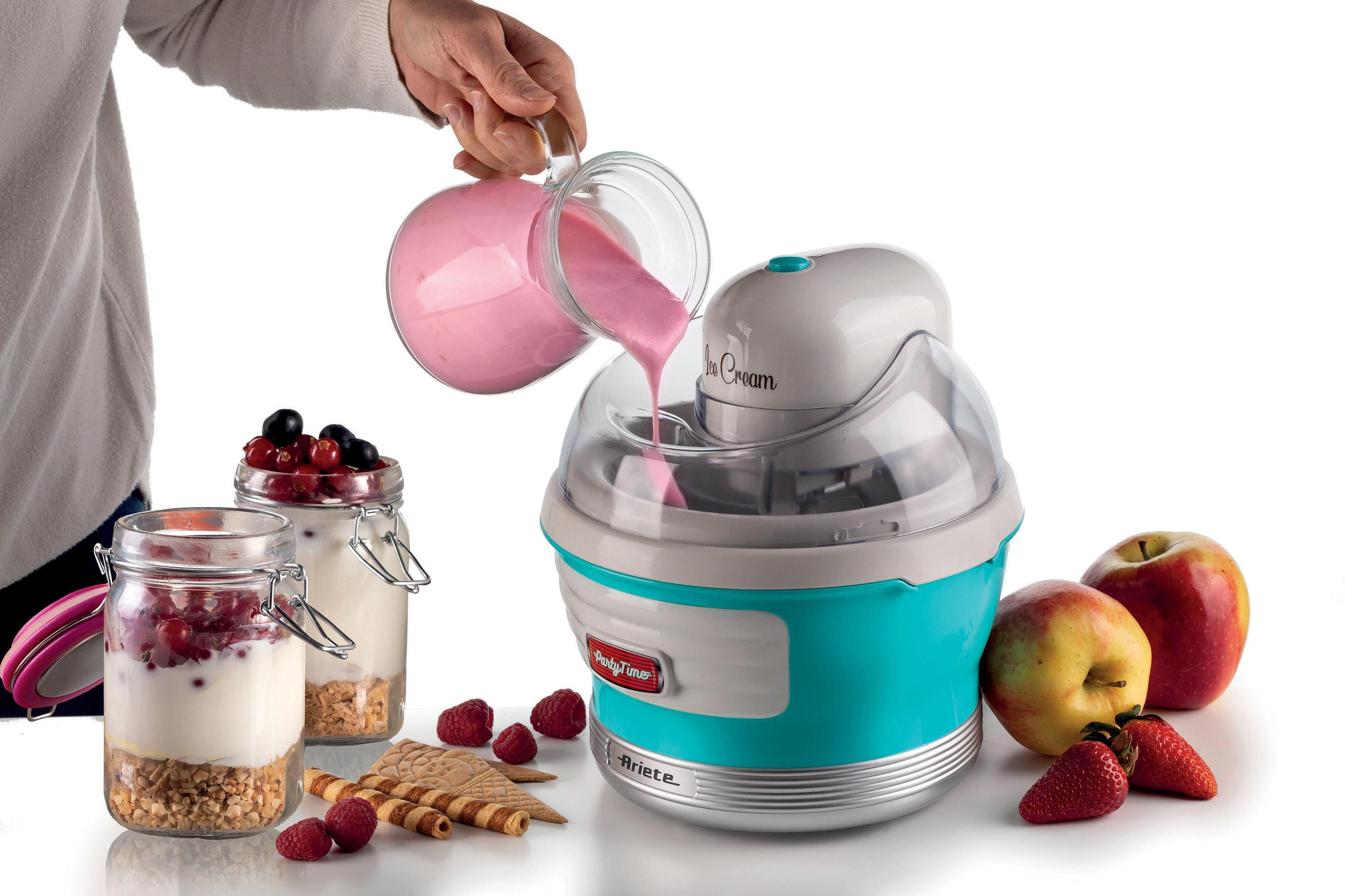 Frau gießt rosa Flüssigkeit in eine Eismaschine. Äpfel und Beeren sind zu sehen.