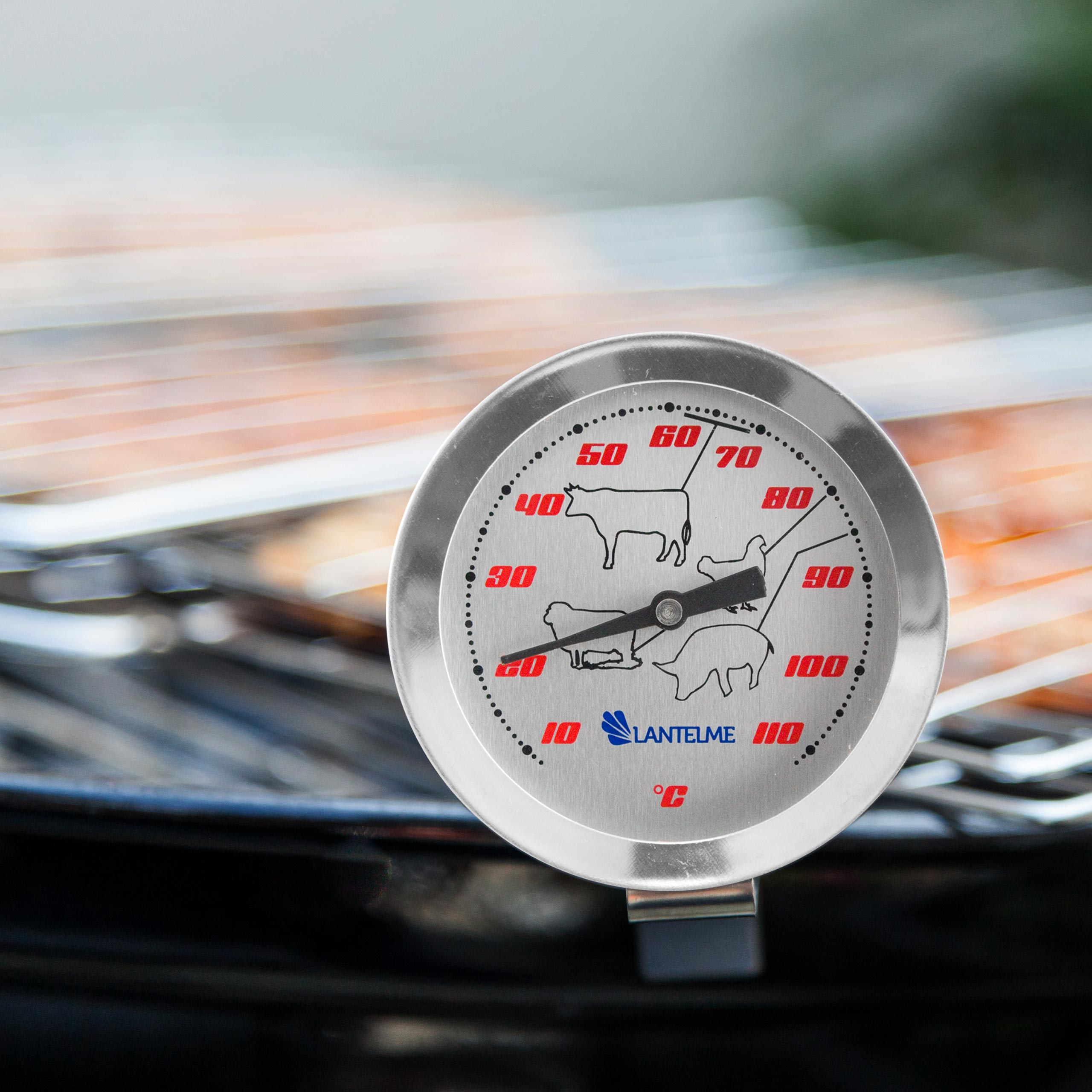 Ein Grillthermometer, das die Temperatur anzeigt, über einem Grill mit Essen platziert. Zeigt verschiedene Fleischsymbole.