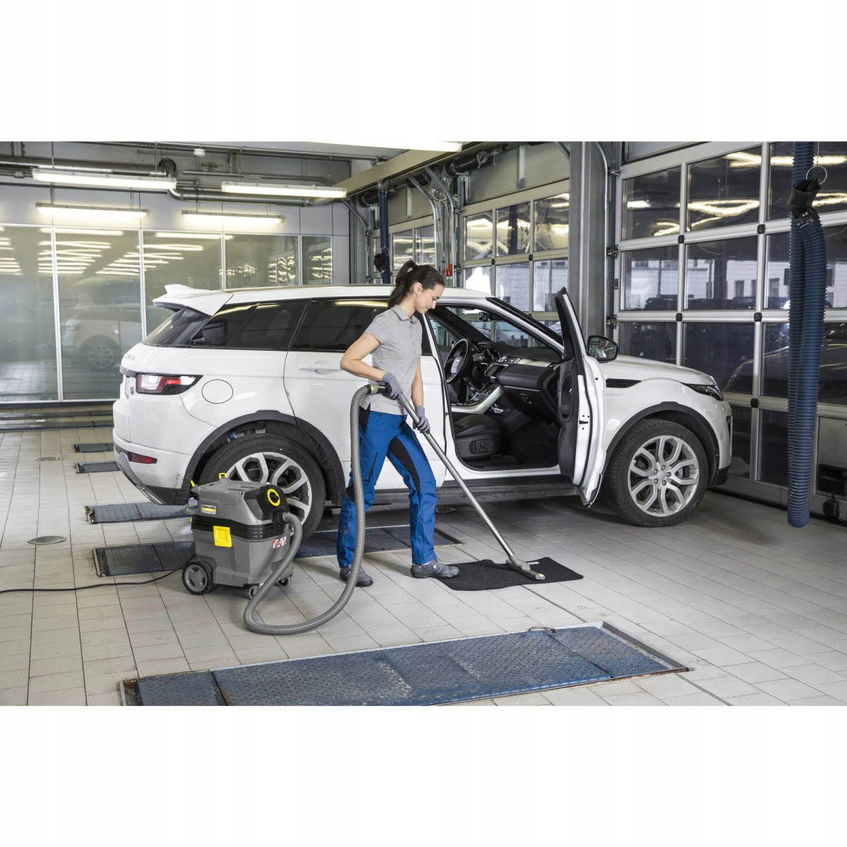 Kobieta odkurza białe SUV w garażu, używając odkurzacza.