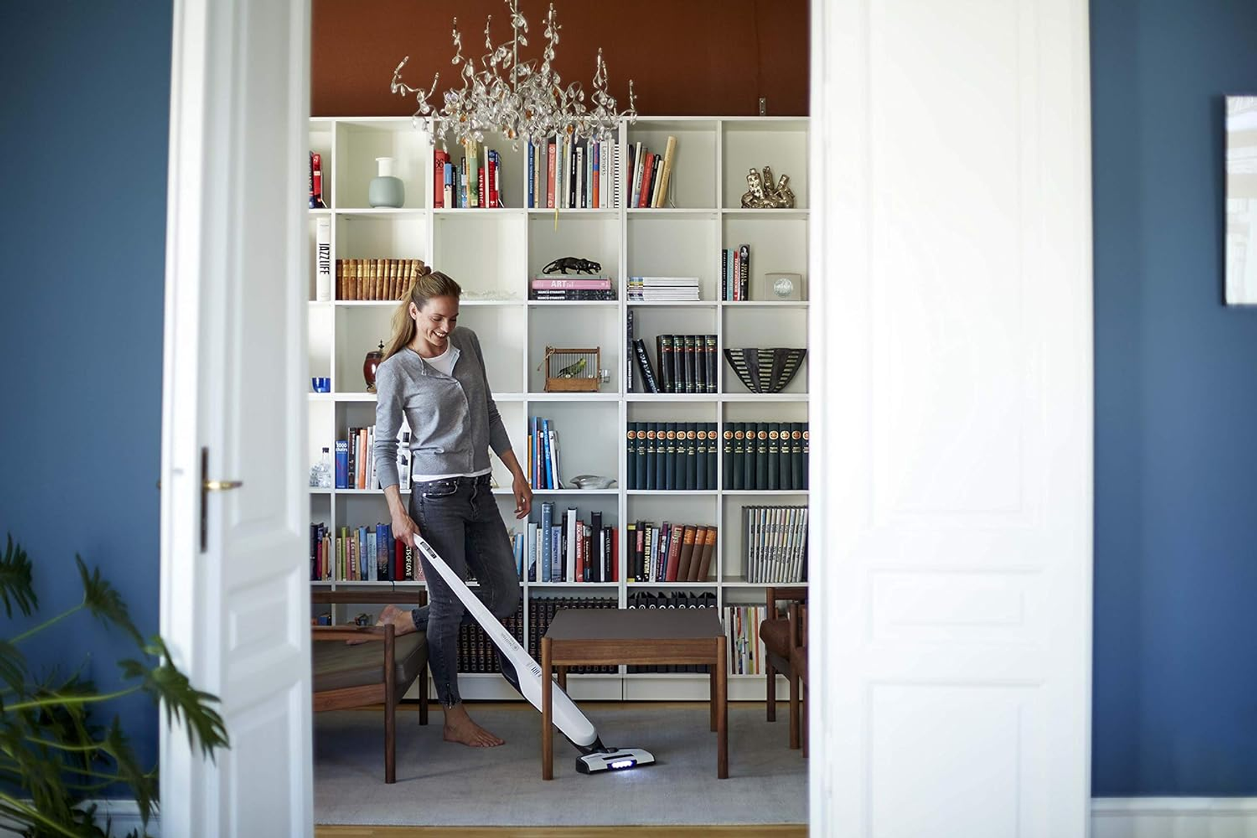 Femme passant l'aspirateur dans une pièce. Étagères de livres et lustre en arrière-plan.