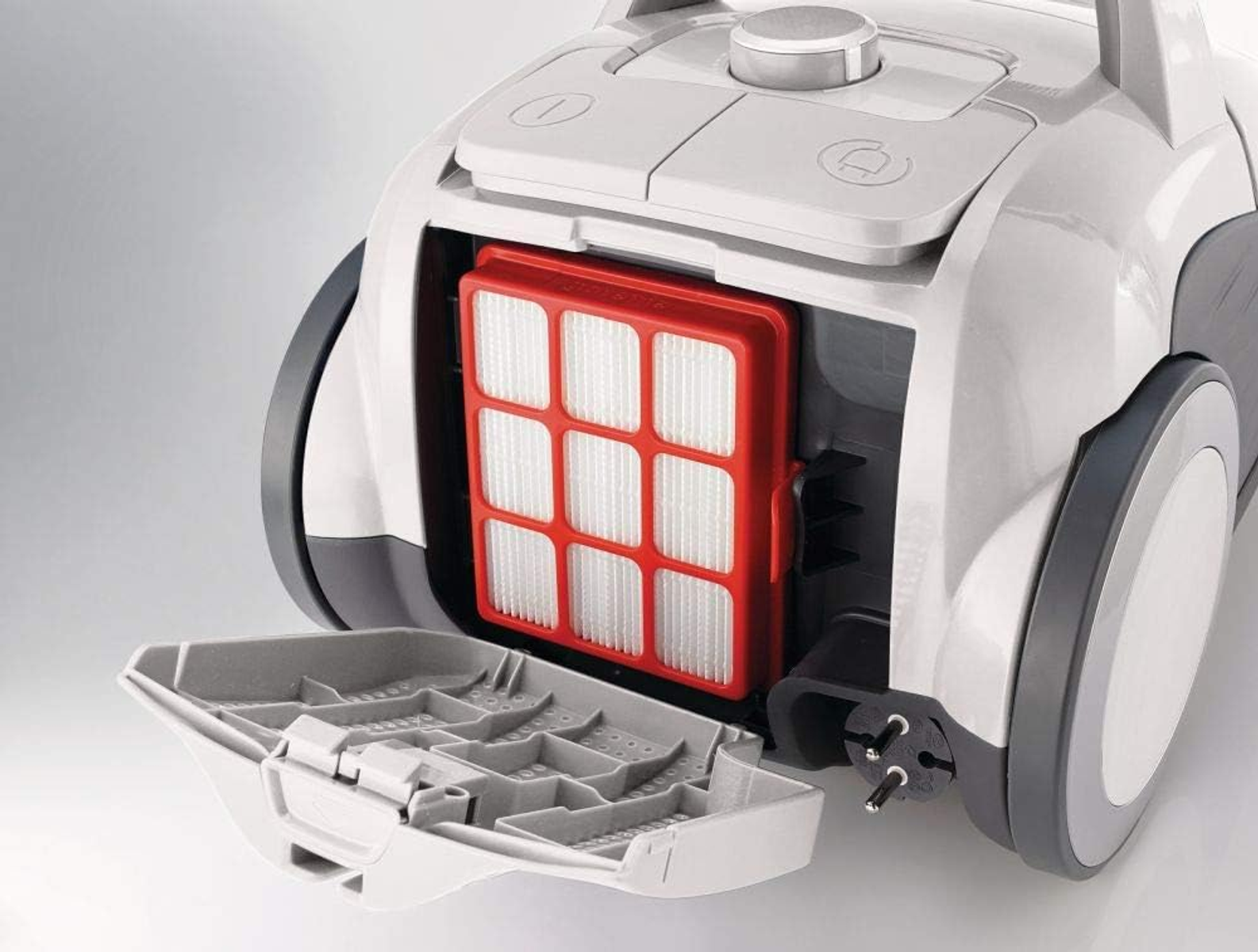 Odkurzacz z otwartą komorą, pokazujący czerwony filtr, na białym tle, zbliżenie.