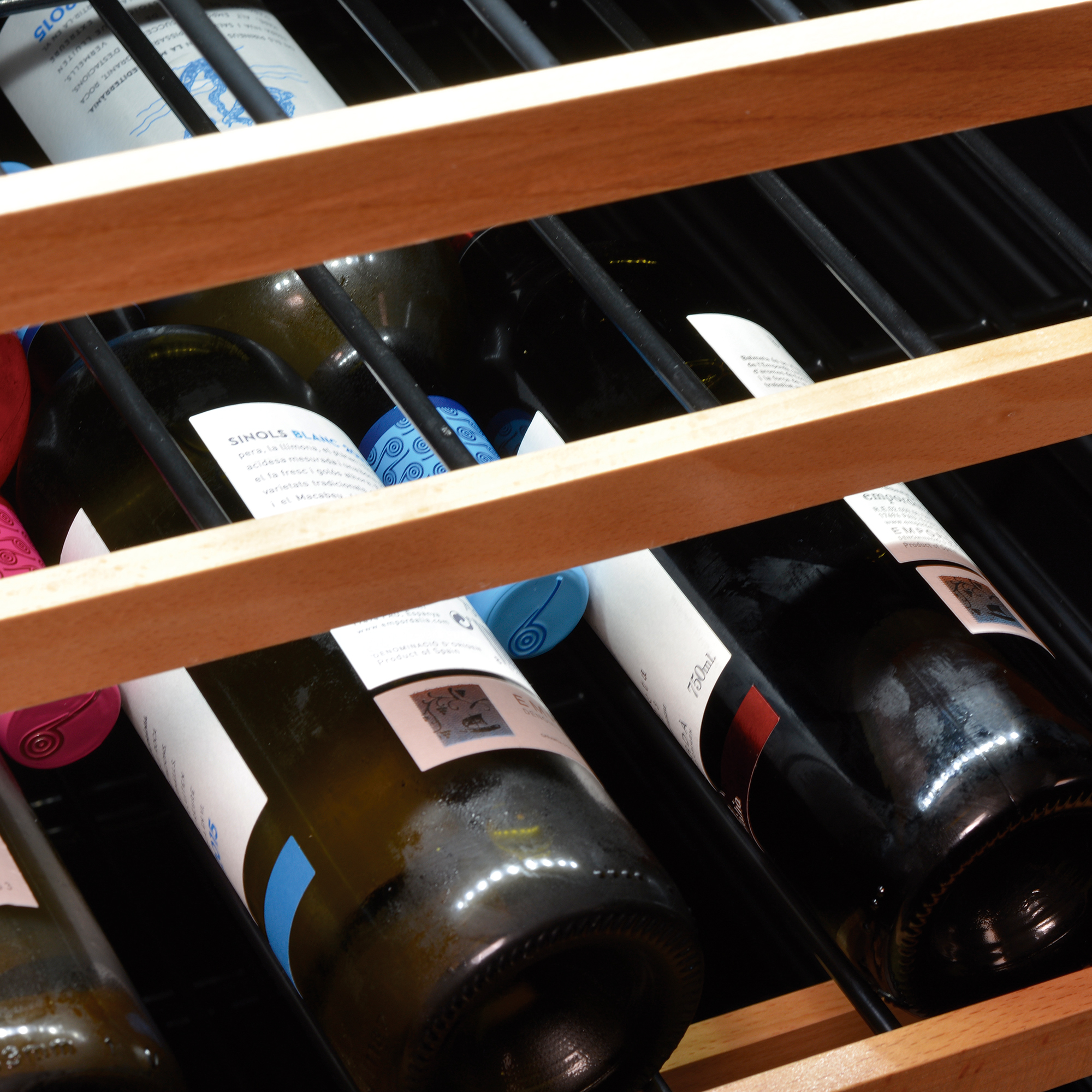Primer plano de botellas de vino en una vinoteca. Estantes de madera sujetan las botellas en ángulo.