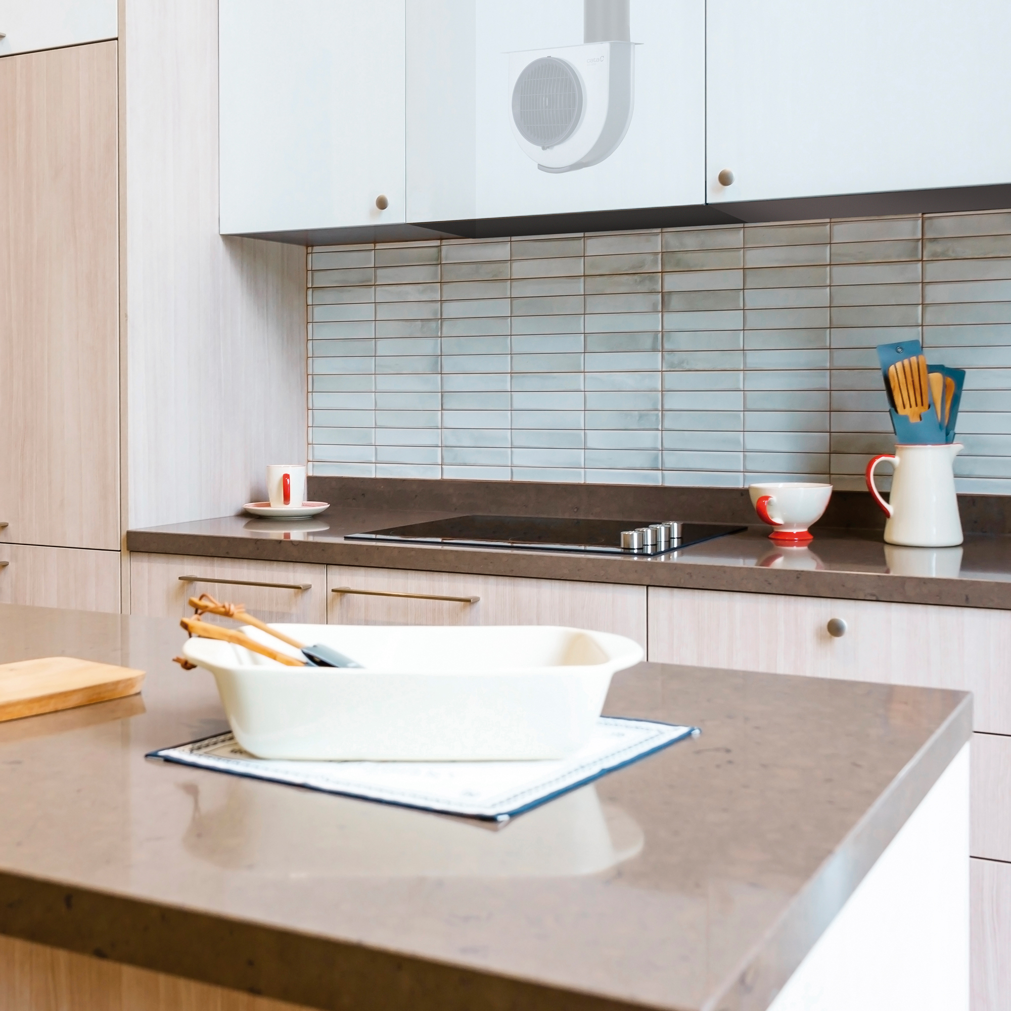Encimera de cocina con una fuente para horno, utensilios y una campana extractora arriba.