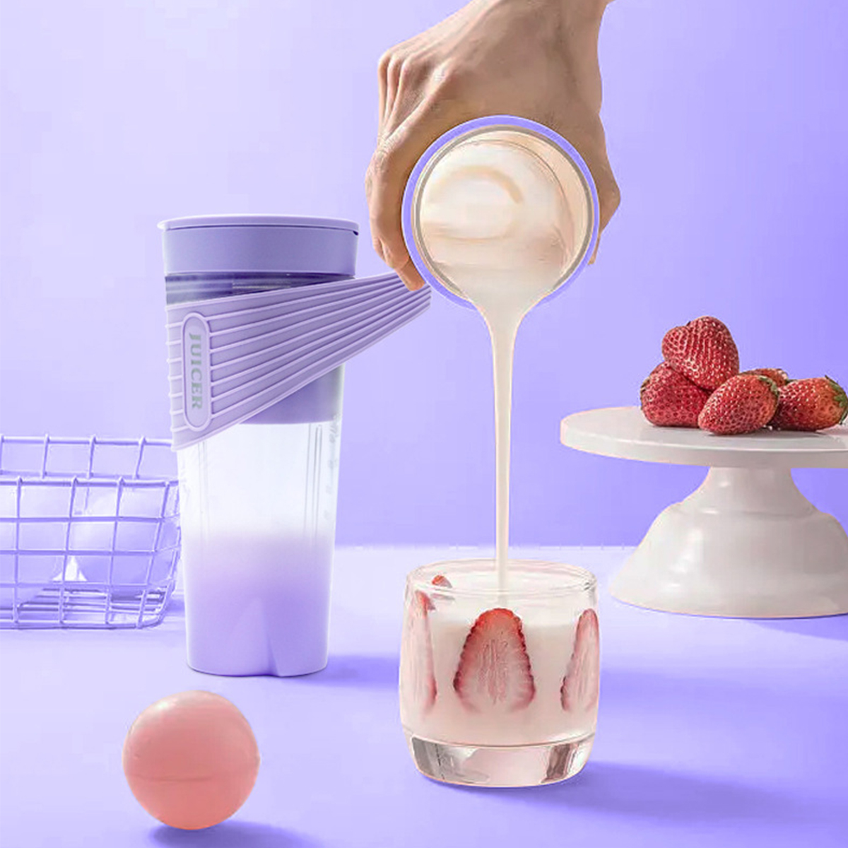 Eine Person gießt Flüssigkeit aus einem Entsafter in ein Glas mit Erdbeeren. Lila Entsafter und eine rosa Kugel sichtbar.