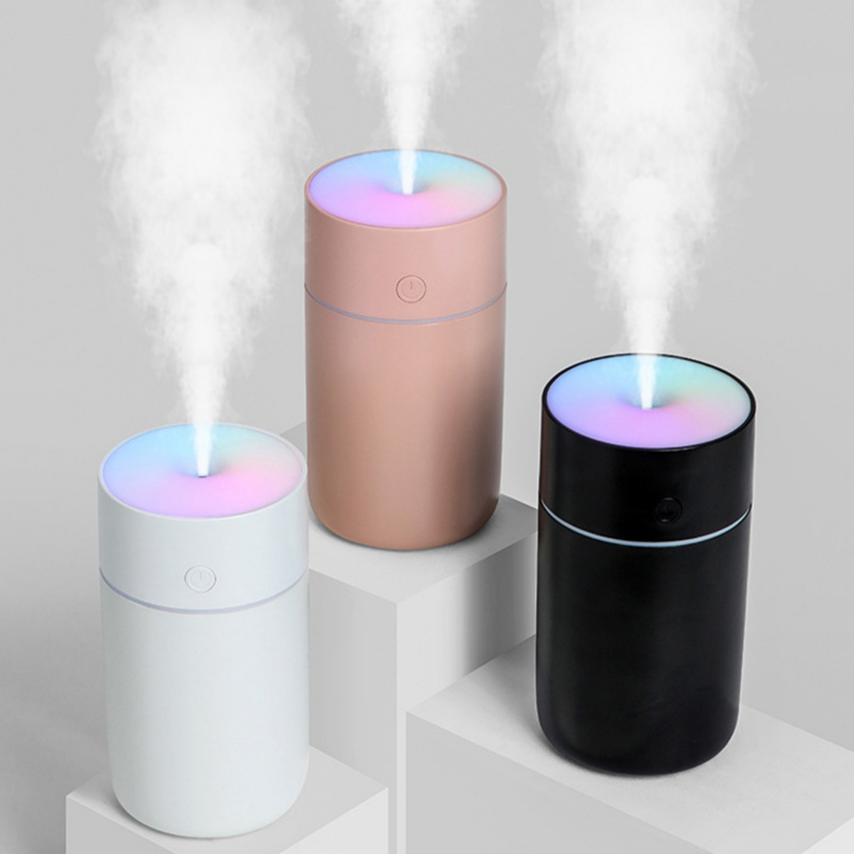 Drei Luftbefeuchter in Weiß, Rosa und Schwarz, die Dampf mit Regenbogenlichtern ausstoßen.