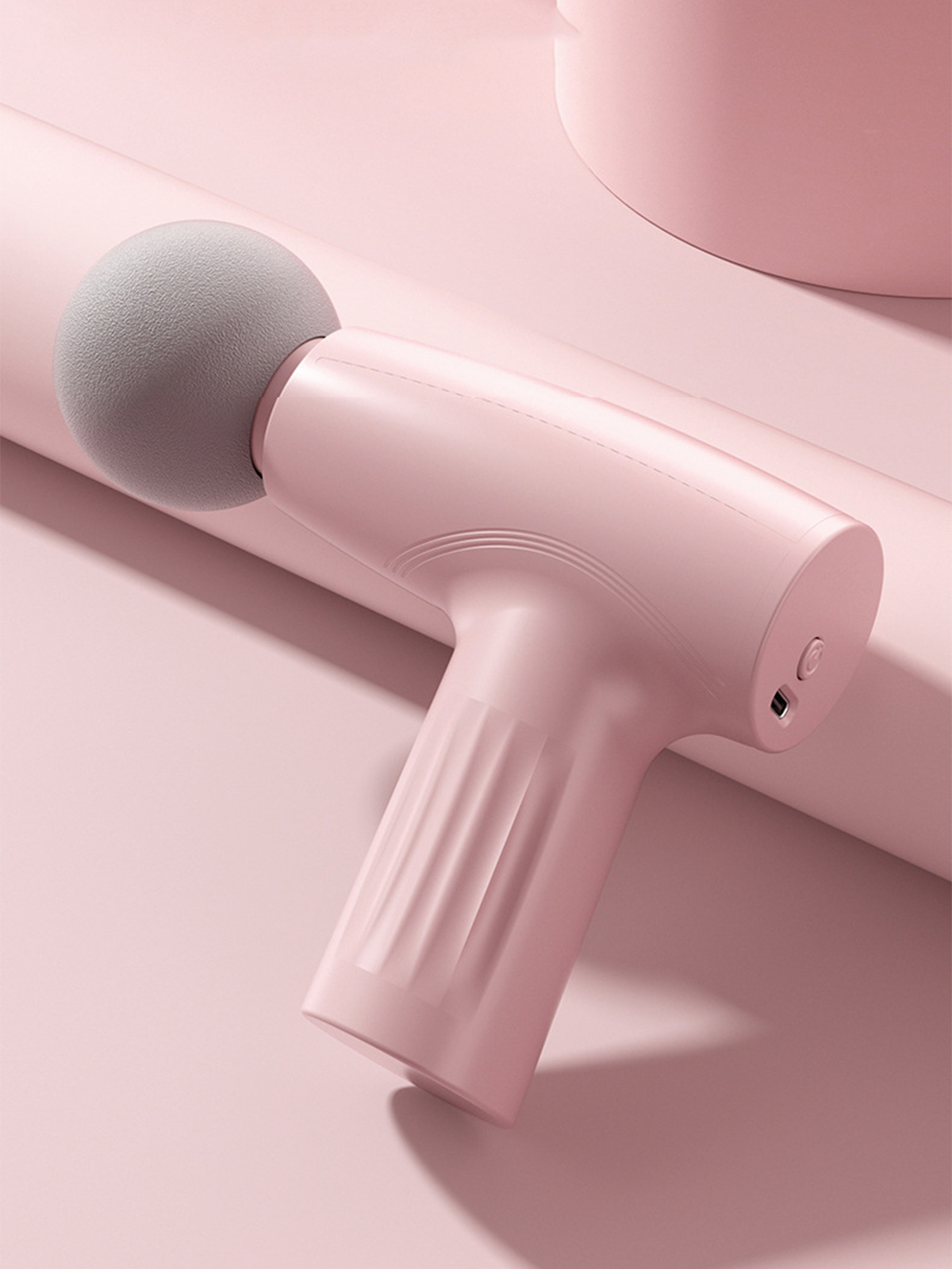 Eine pinkfarbene Massagepistole, ein Massagegerät auf einer pinkfarbenen Oberfläche.