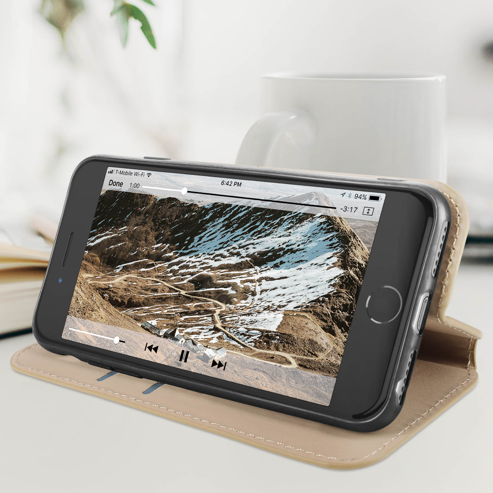 Een smartphone in een hoesje met een berglandschap video, op een tafel met een witte beker.
