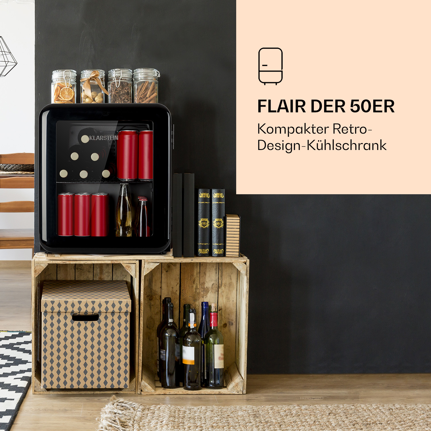 Un mini frigorífico negro de estilo retro con latas rojas y botellas sobre cajas de madera. Frascos encima. Texto: Flair Der 50er.