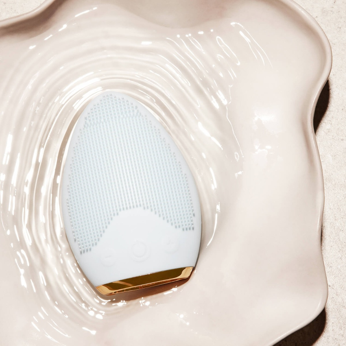 Weiße Gesichtsreinigungsbürste in einer weißen, wellenförmigen, muschelartigen Schale. Wasser.