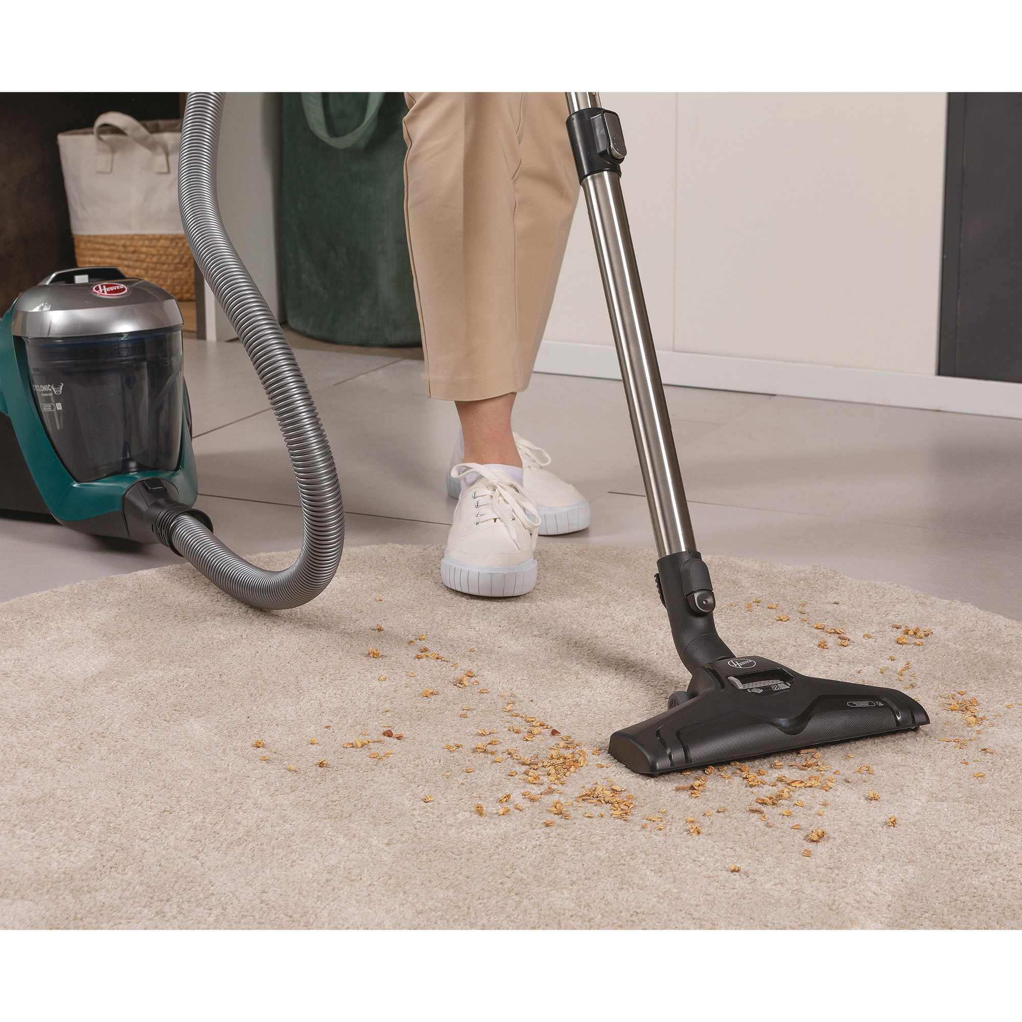 Osoba odkurzająca beżowy dywan turkusowym odkurzaczem.