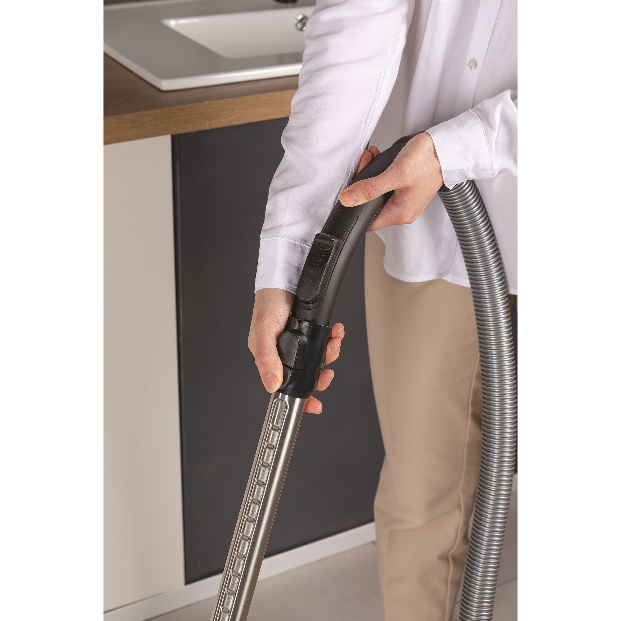 Dłonie osoby trzymającej uchwyt odkurzacza, ze srebrną rurą przedłużającą.