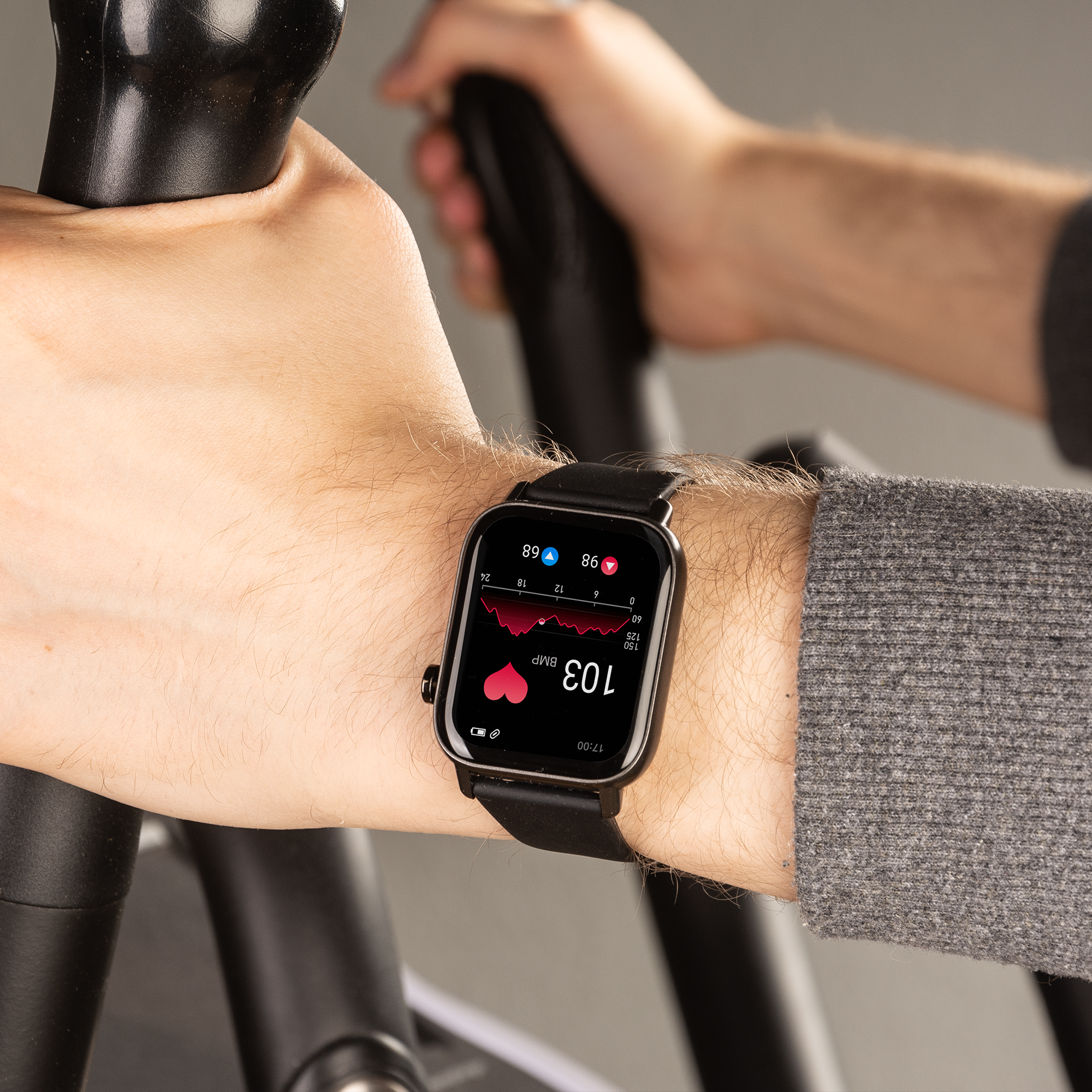 Handgelenk einer Person mit Smartwatch, die Herzfrequenzdaten während des Trainings auf einem Crosstrainer anzeigt.
