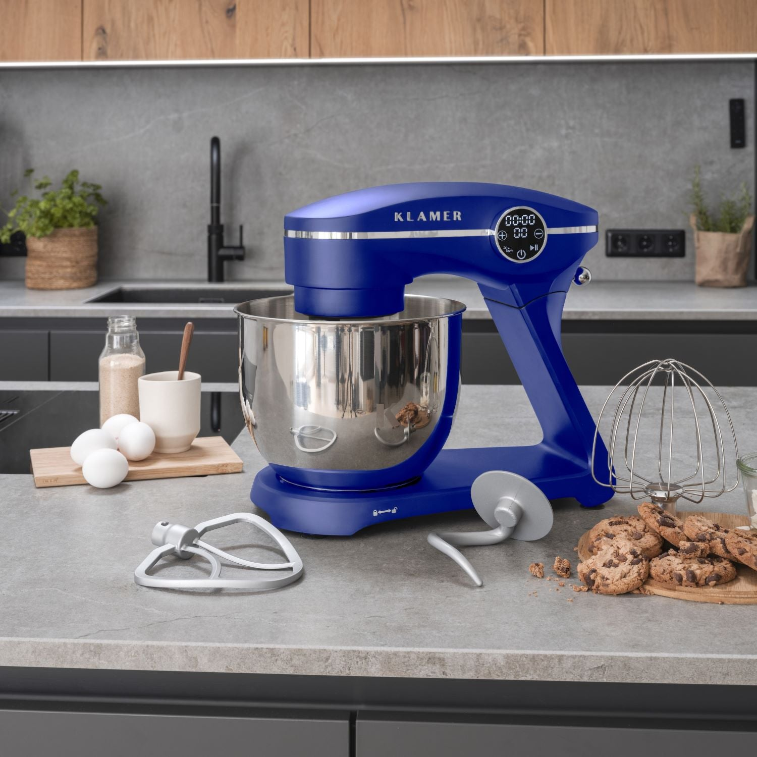Ein blauer Küchenmixer mit Edelstahlschüssel, Zutaten und Zubehör auf einer Küchentheke.