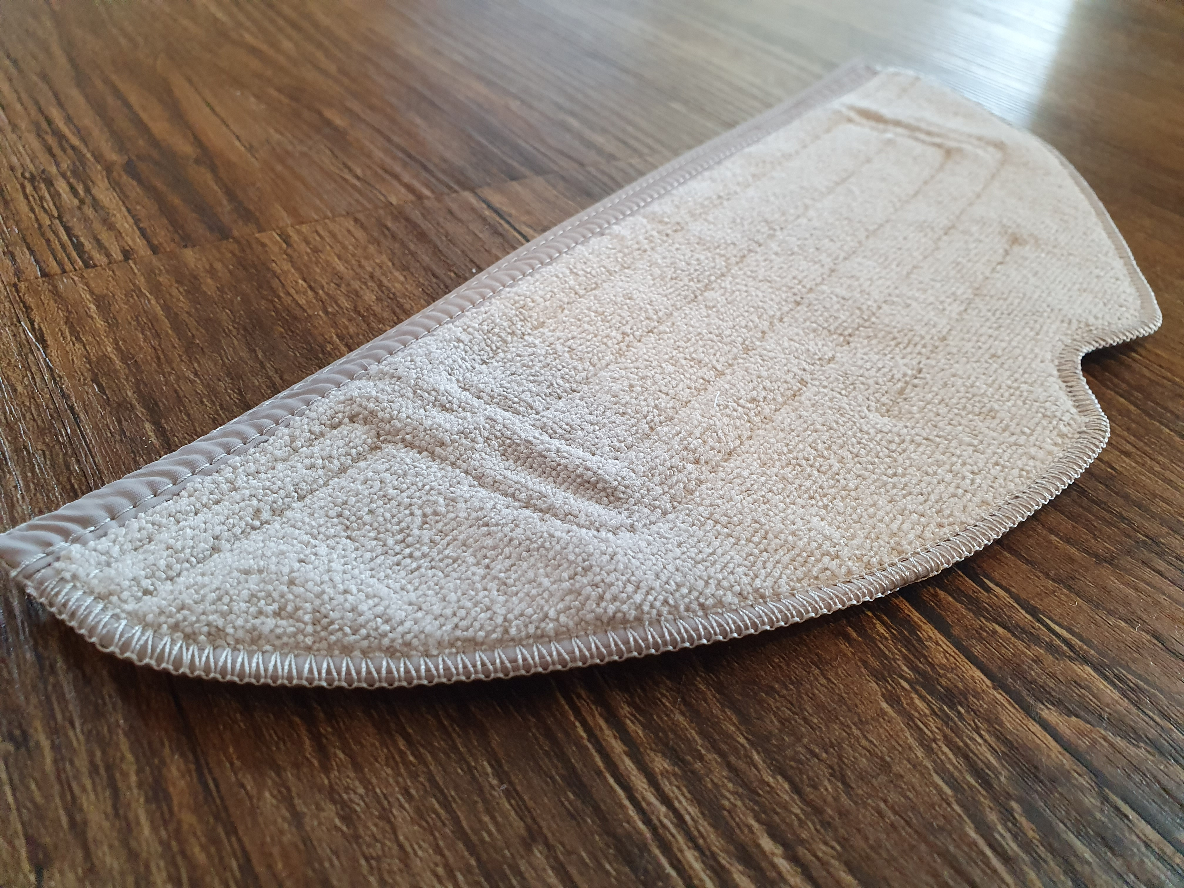 Ein hellbeige Mikrofaser-Wischmopp-Pad liegt auf einem Holzboden. Das Pad hat eine strukturierte Oberfläche.