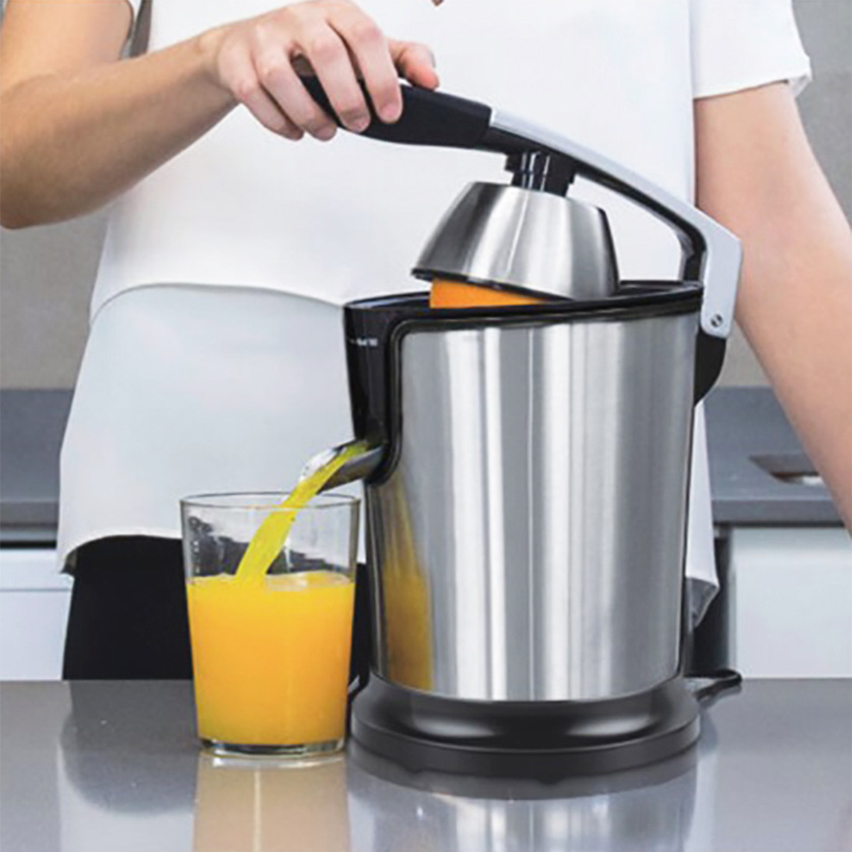 Eine Frau presst Orangensaft in ein Glas mit einer Metallpresse. Ein Glas Saft steht daneben.