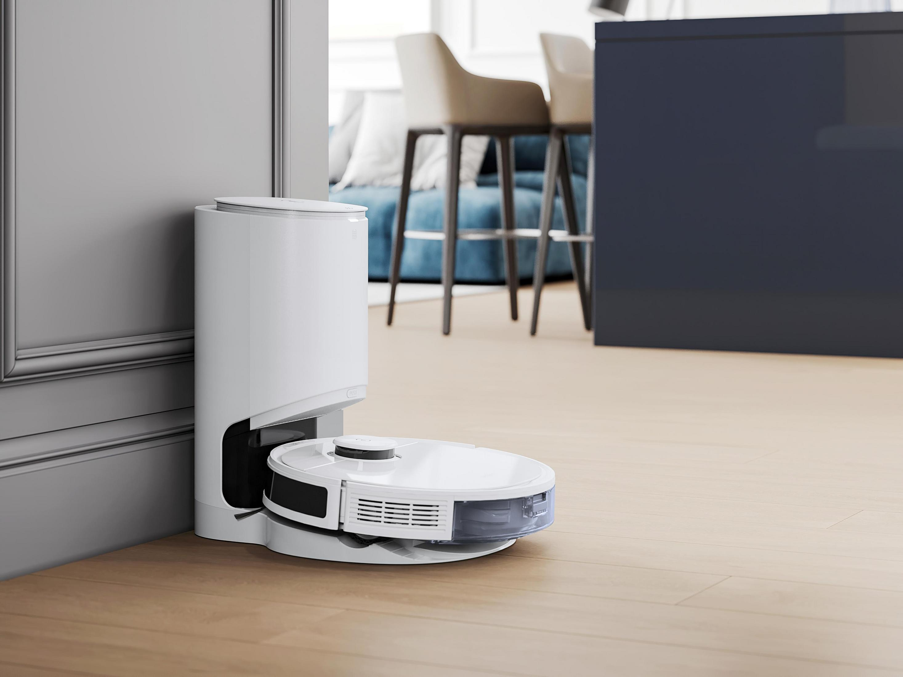 Aspirapolvere robotico bianco e base di ricarica in una stanza con pavimento in legno.