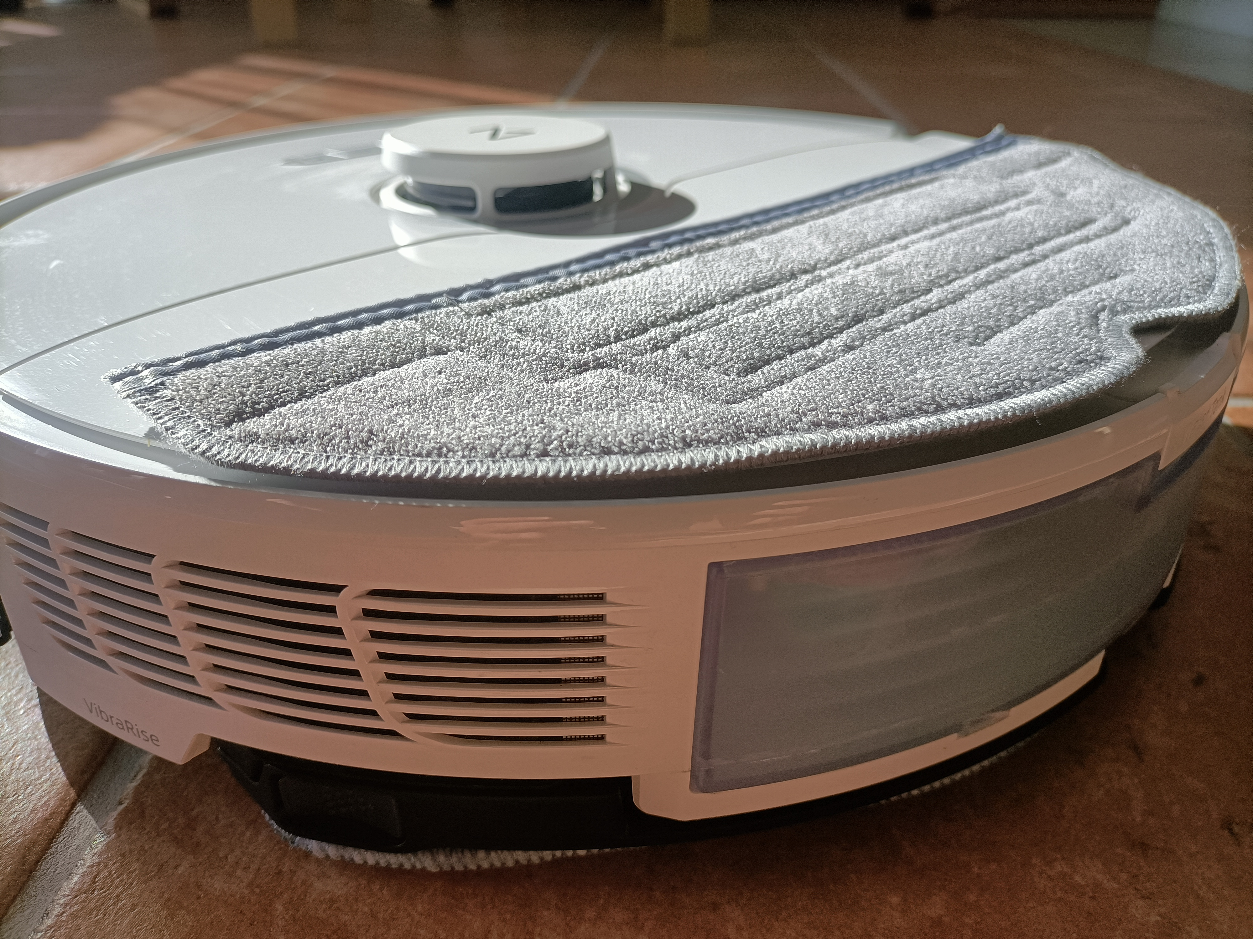 Ein weißer und grauer Roboter-Staubsauger auf einem Boden. Es hat ein Reinigungspad.
