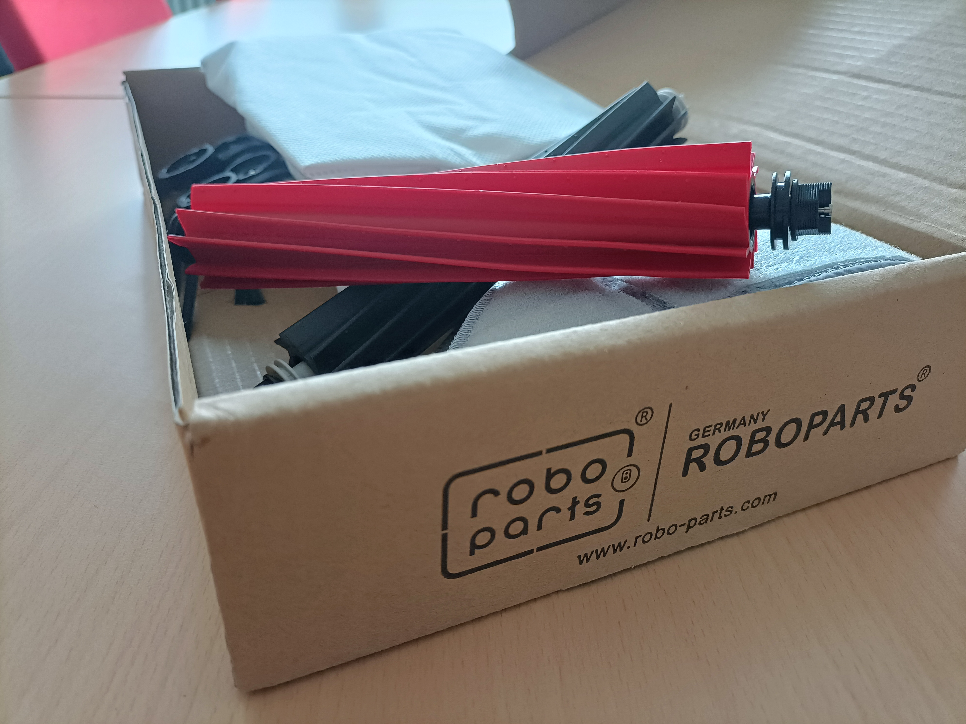 Boîte de pièces de nettoyage pour aspirateur robot, avec une brosse rouge.