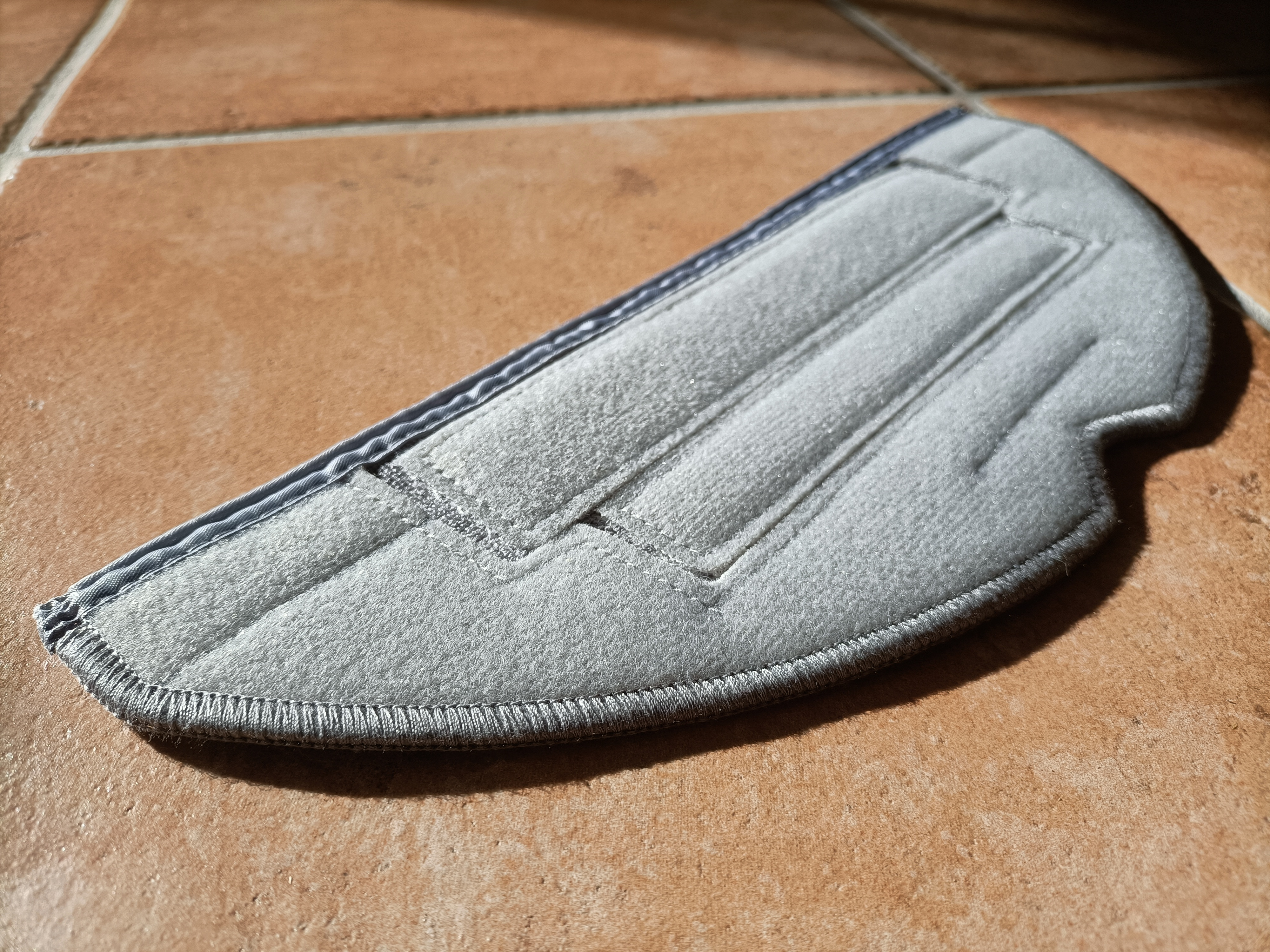 Un tampon de vadrouille en microfibre grise sur un sol en carrelage marron, éclairé par la lumière du soleil. Un gros plan.