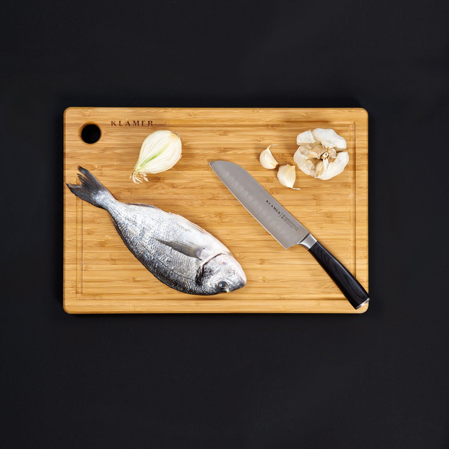 Holzschneidebrett mit Fisch, Zwiebel, Knoblauch und Messer. Schwarzer Hintergrund.
