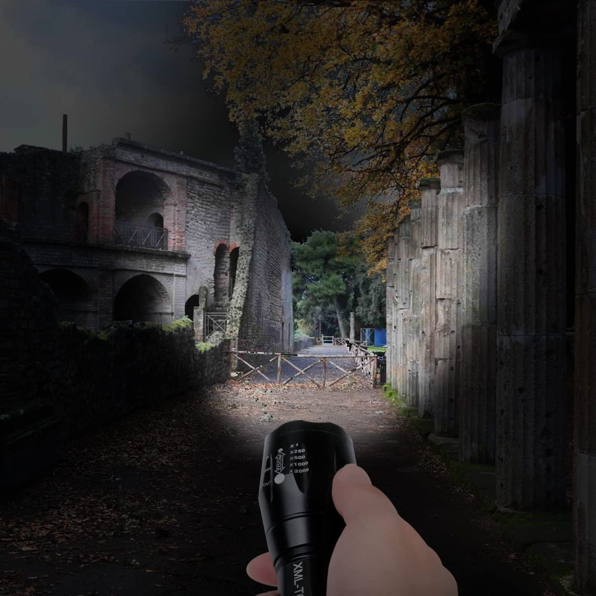 Eine Hand hält eine schwarze Taschenlampe, die eine antike Ruine bei Nacht beleuchtet. Der Strahl leuchtet nach vorne.