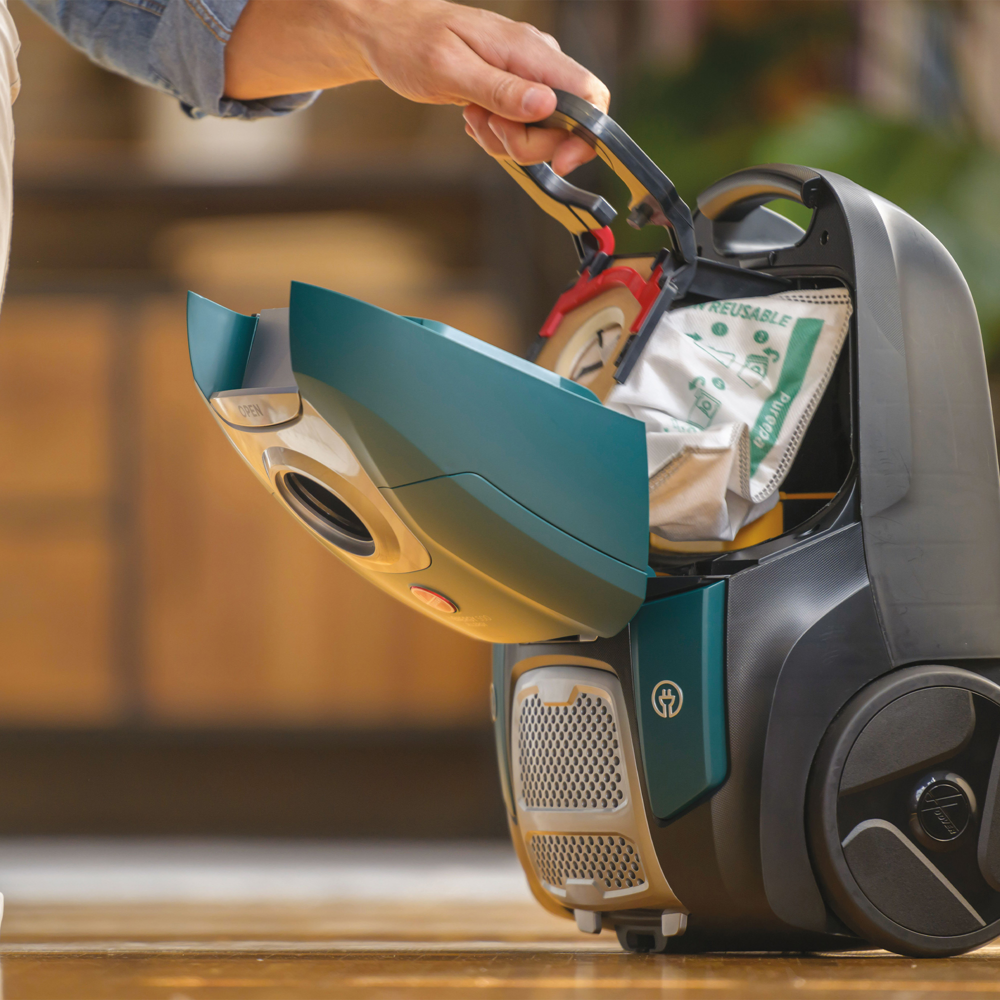 Ręka otwierająca komorę odkurzacza, odsłaniając worek na kurz.