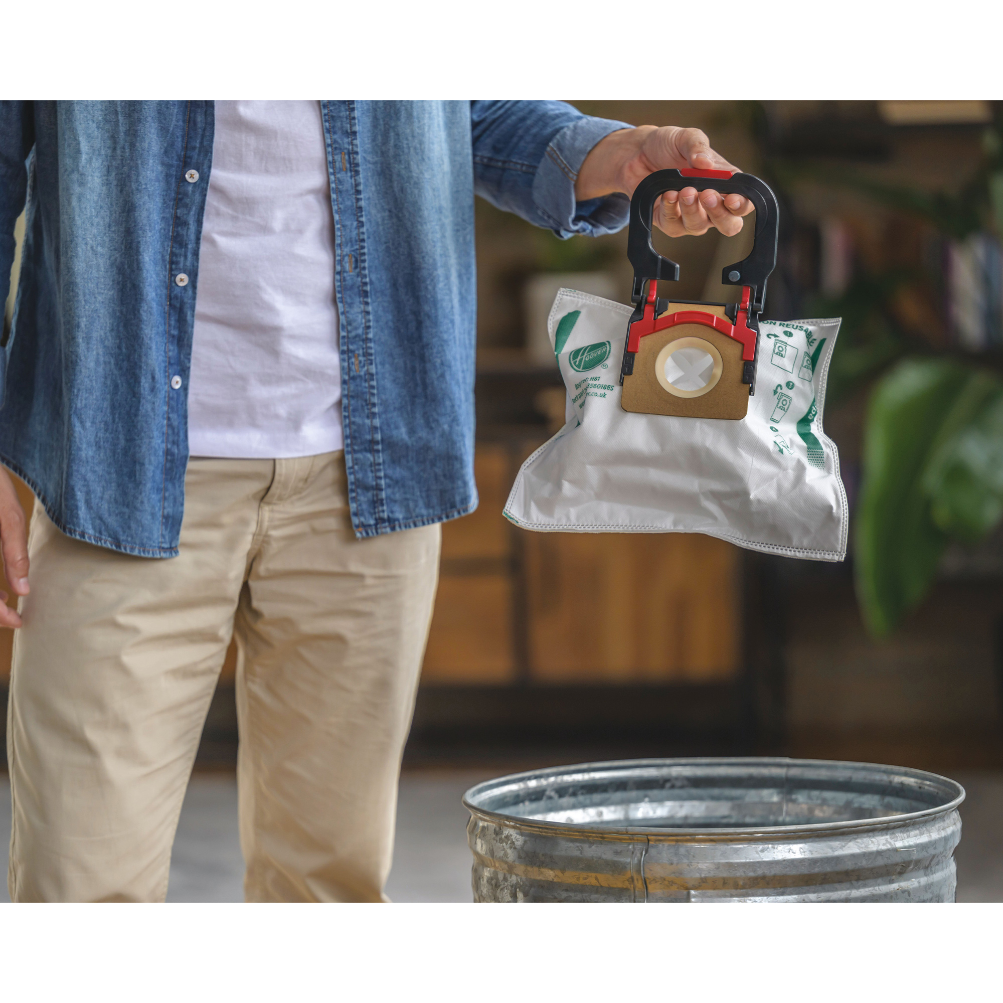 Osoba trzymająca biały worek do odkurzacza przymocowany do uchwytu, nad metalowym koszem na śmieci.