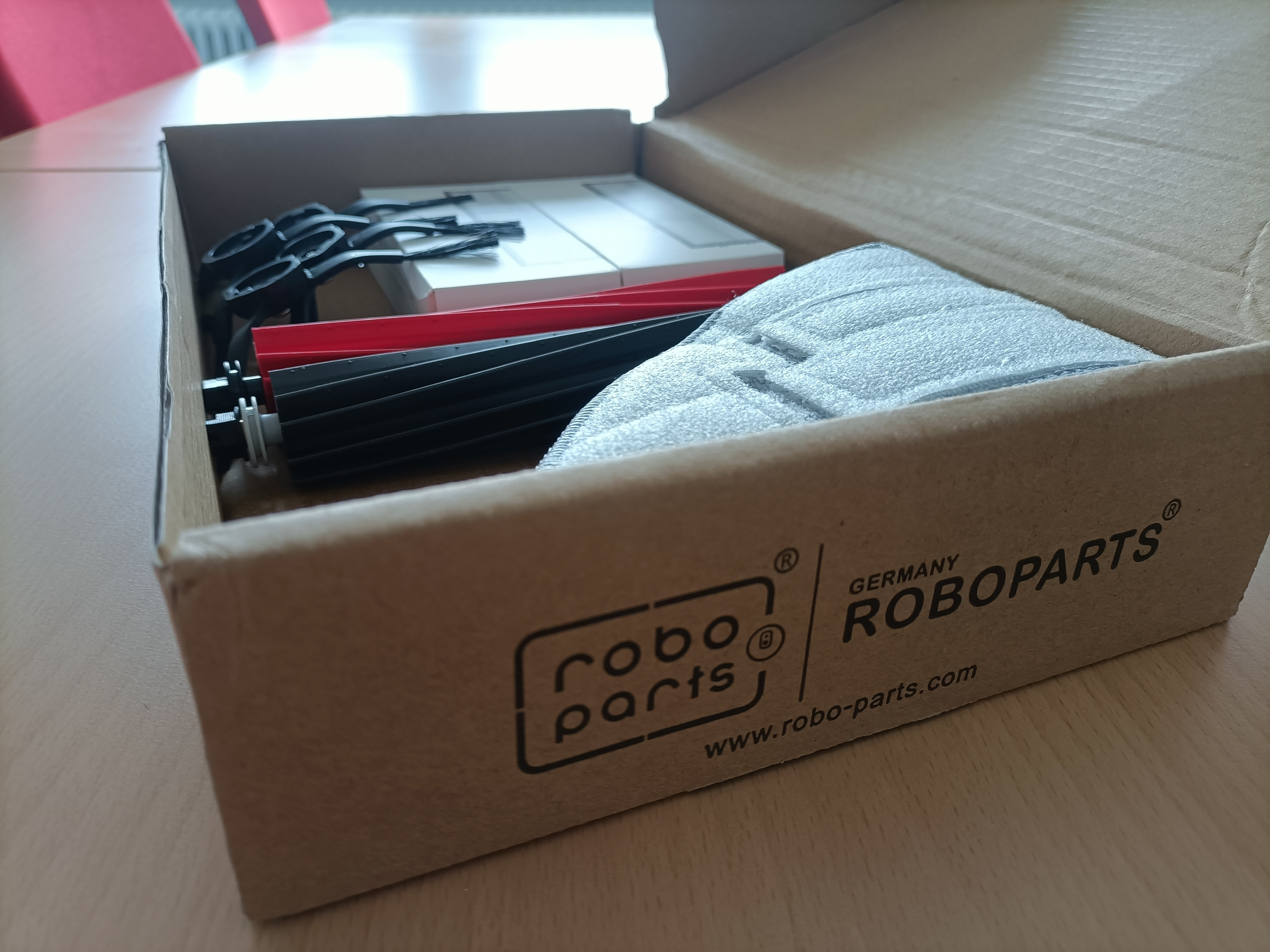 Scatola di cartone aperta contenente parti di robot e accessori per la pulizia.