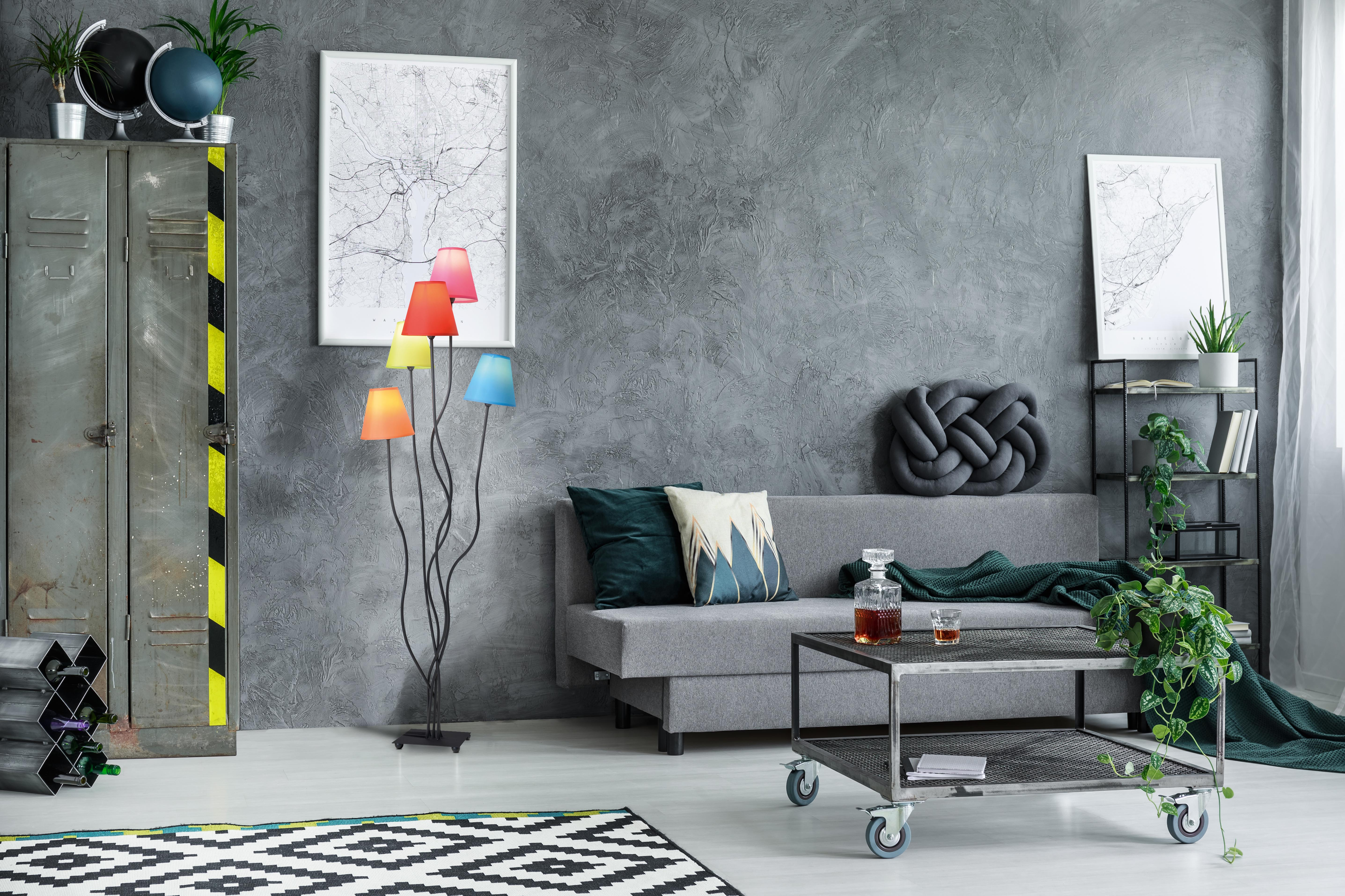 Ein Wohnzimmer mit grauen Wänden, einem Sofa, einer Lampe mit farbigen Schirmen und einem gemusterten Teppich.