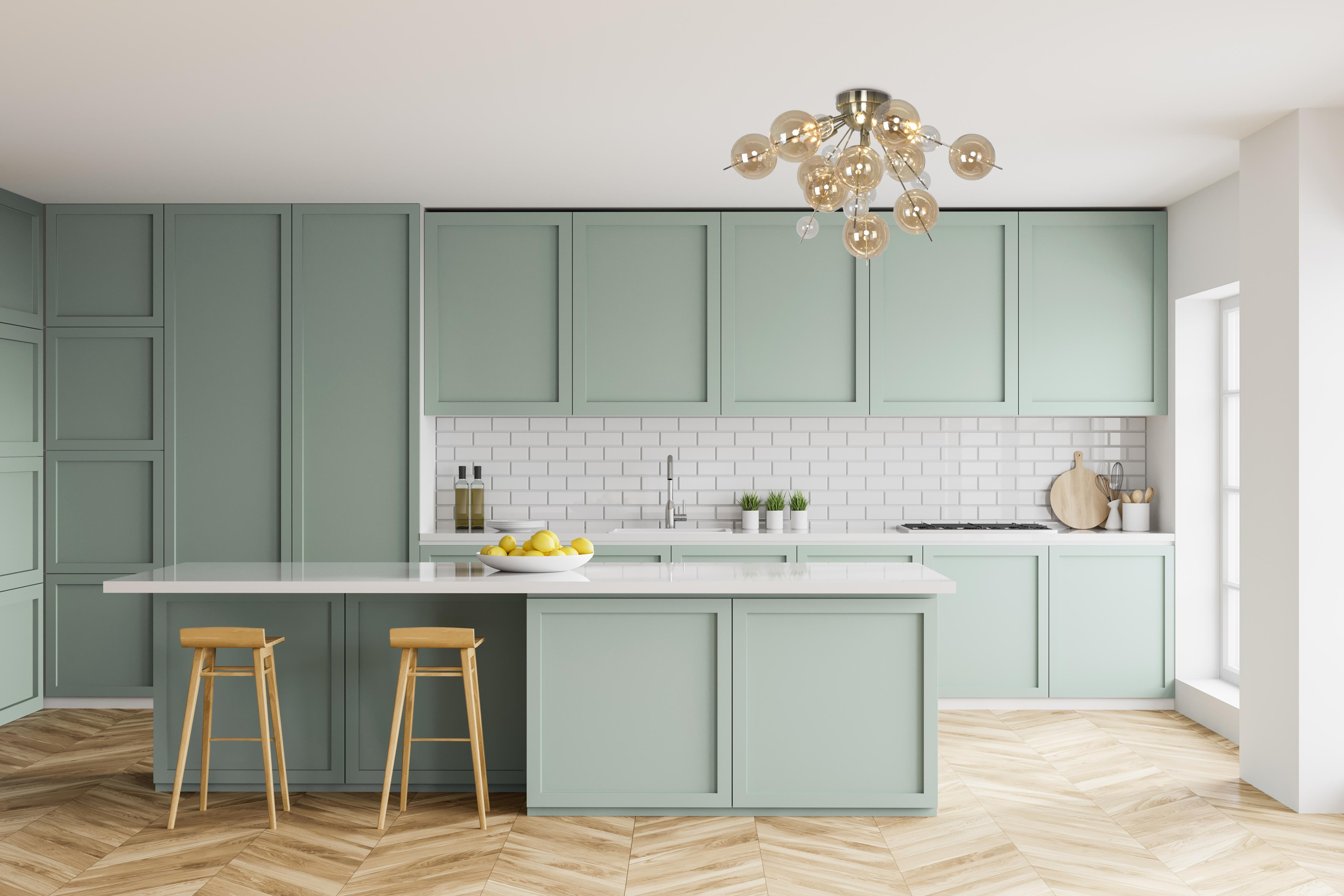 Une cuisine moderne avec des armoires vert menthe, des comptoirs blancs et un luminaire.
