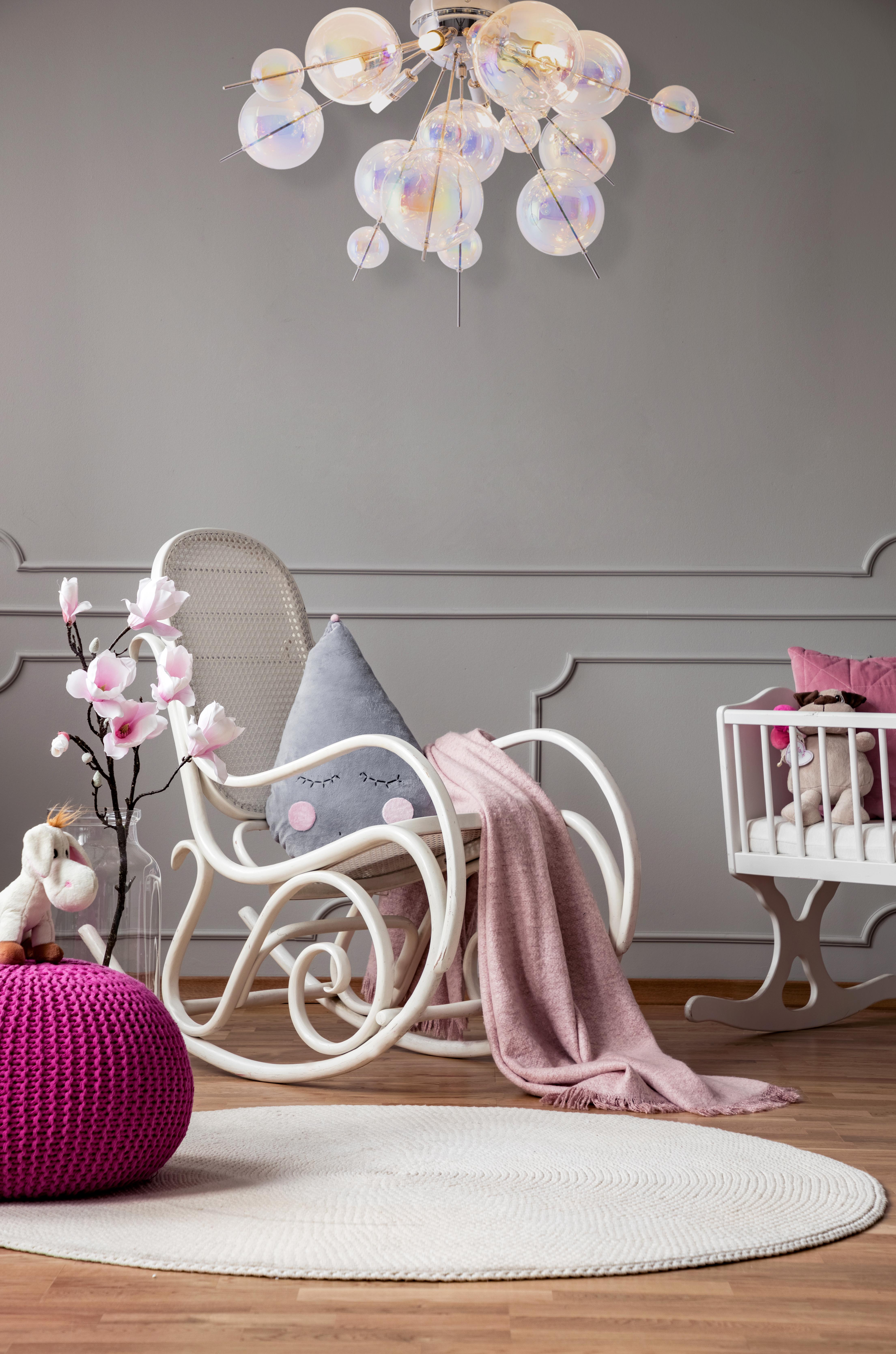 Ein Kinderzimmer mit einem weißen Schaukelstuhl, einer rosa Decke und einer Babywiege, dekoriert mit einem Kronleuchter.