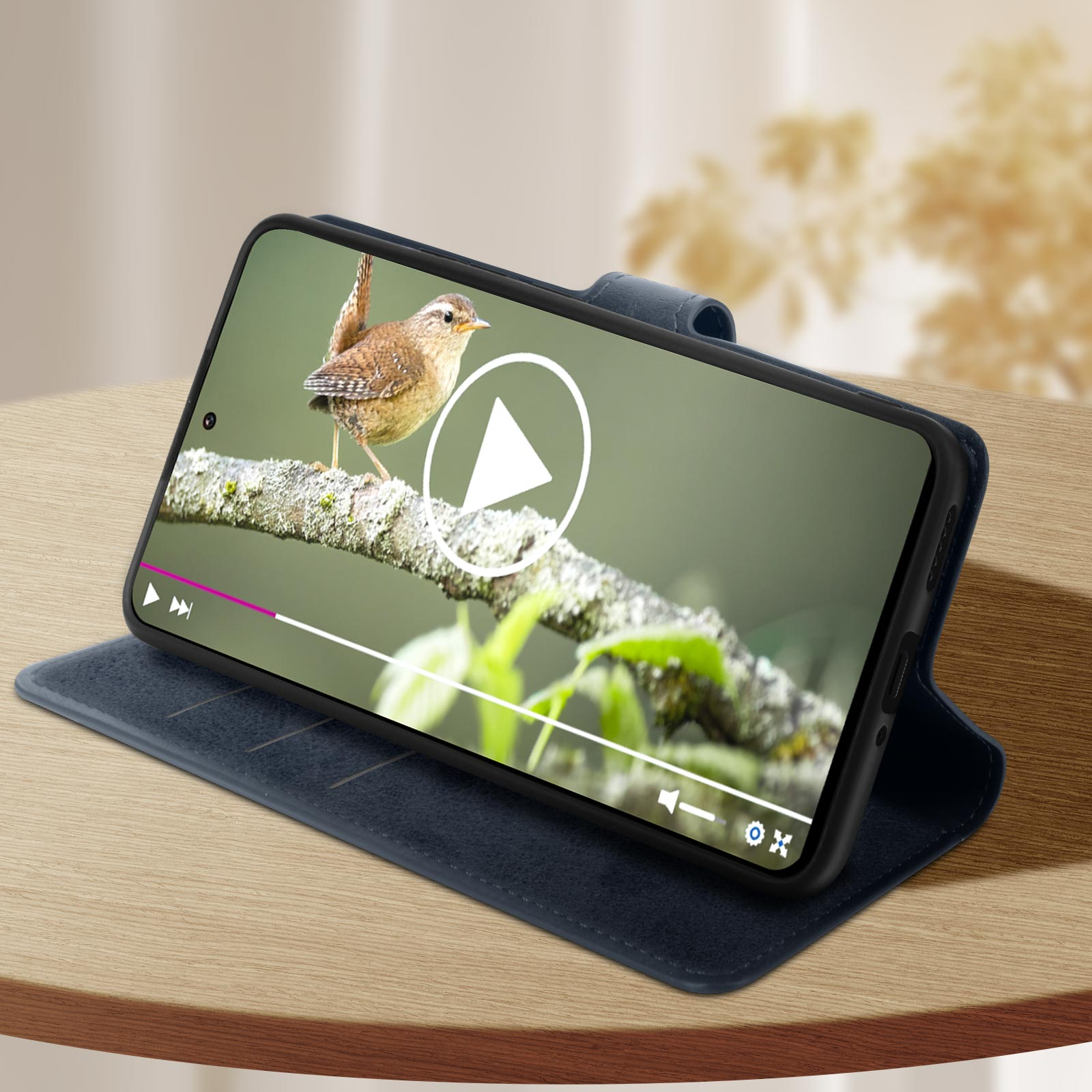 Ein Telefon in einer blauen Hülle zeigt ein Video eines Vogels auf einem Ast. Das Telefon liegt auf einem Tisch.