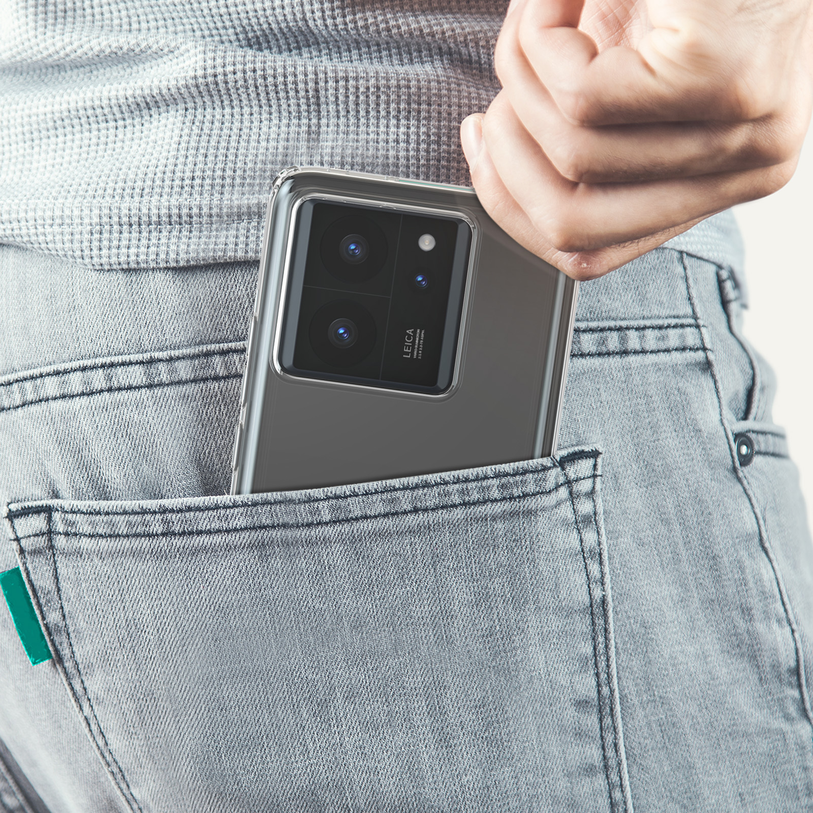 Una mano che mette un telefono nella tasca posteriore di jeans grigio chiaro. Il telefono è in una custodia.