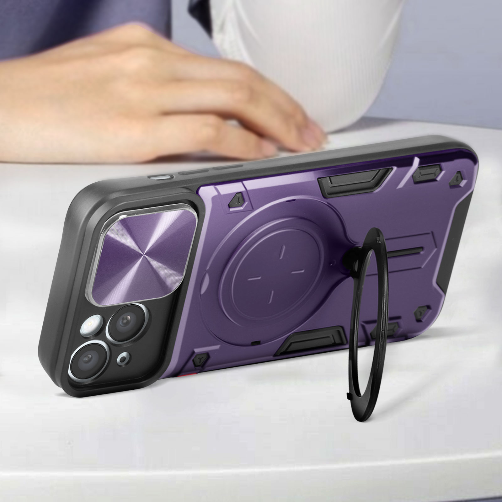 Custodia per telefono viola con supporto ad anello, telefono su superficie bianca. Mano sullo sfondo.