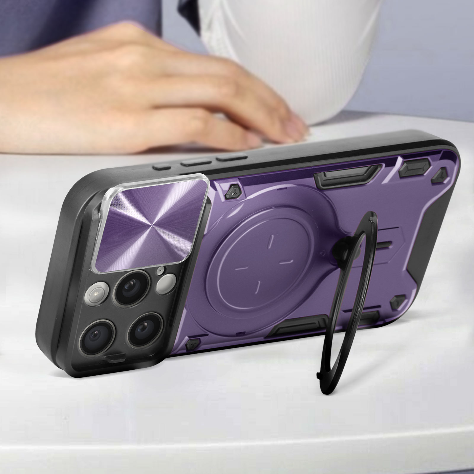 Una custodia per telefono con retro viola, cornice nera e un supporto ad anello. Il telefono è appoggiato su una superficie bianca.
