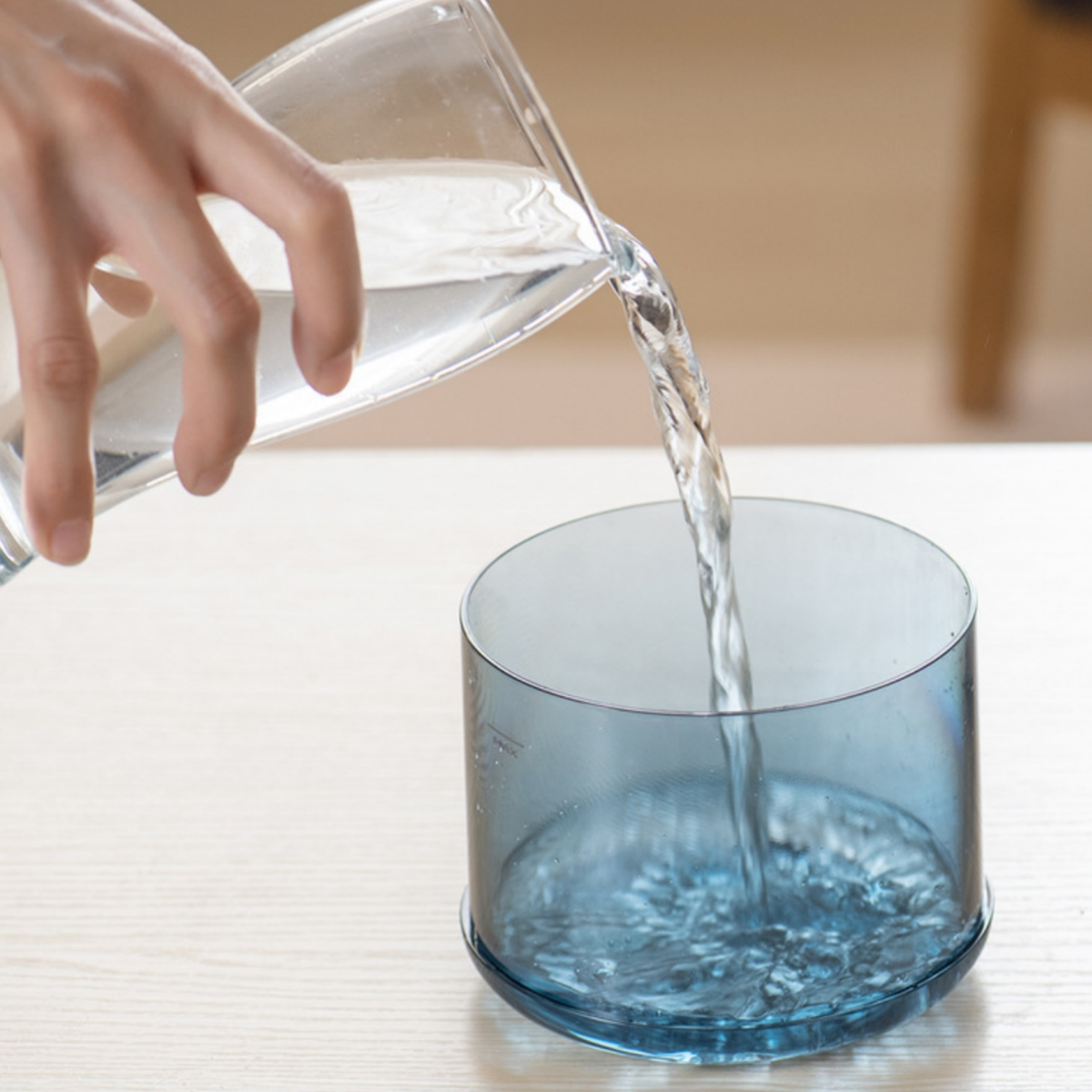 Eine Hand, die Wasser in ein blaues transparentes Glas gießt. Das Wasser fließt in das Glas.