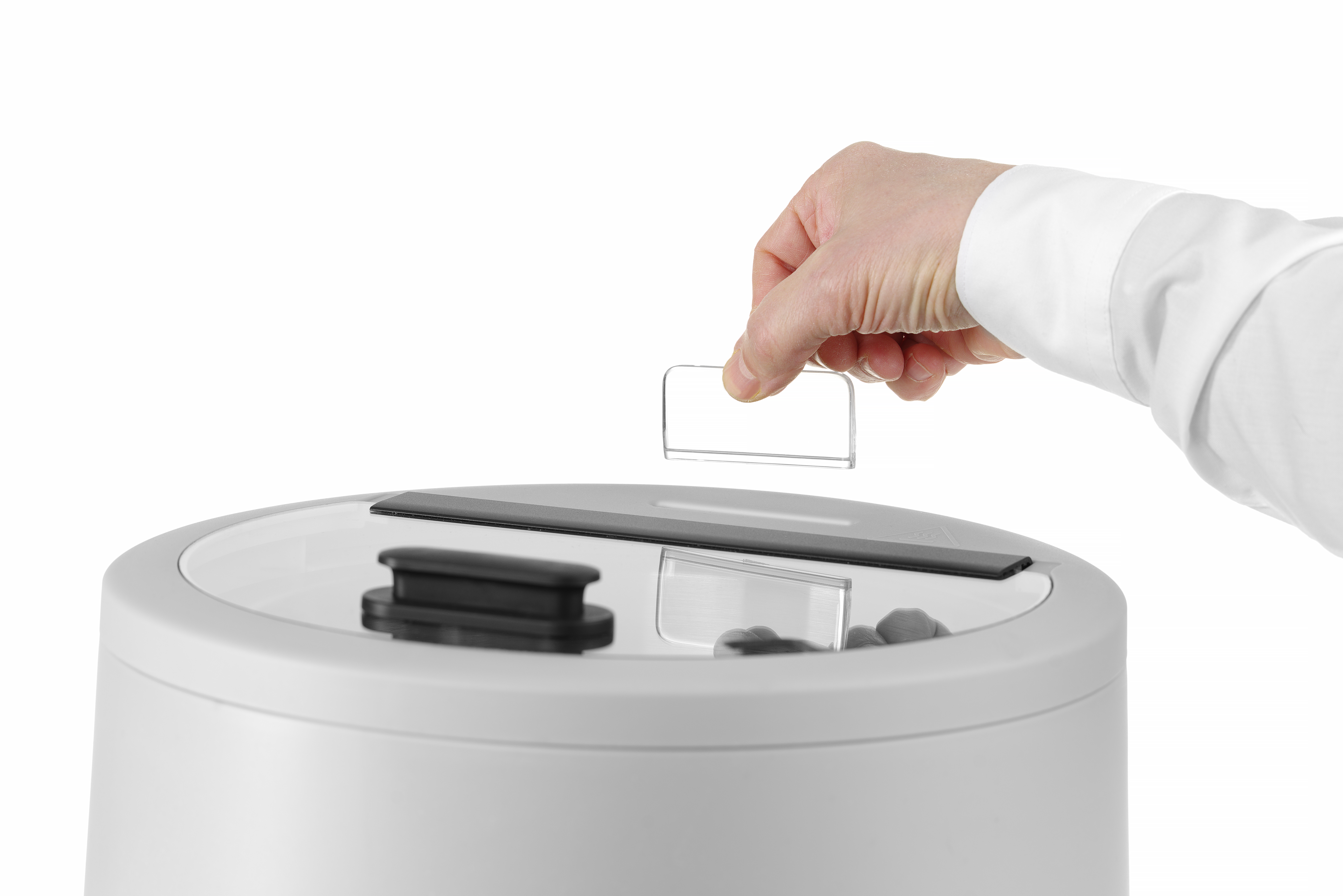 Una mano che inserisce una piccola carta rettangolare in un cestino bianco. Il coperchio è aperto.