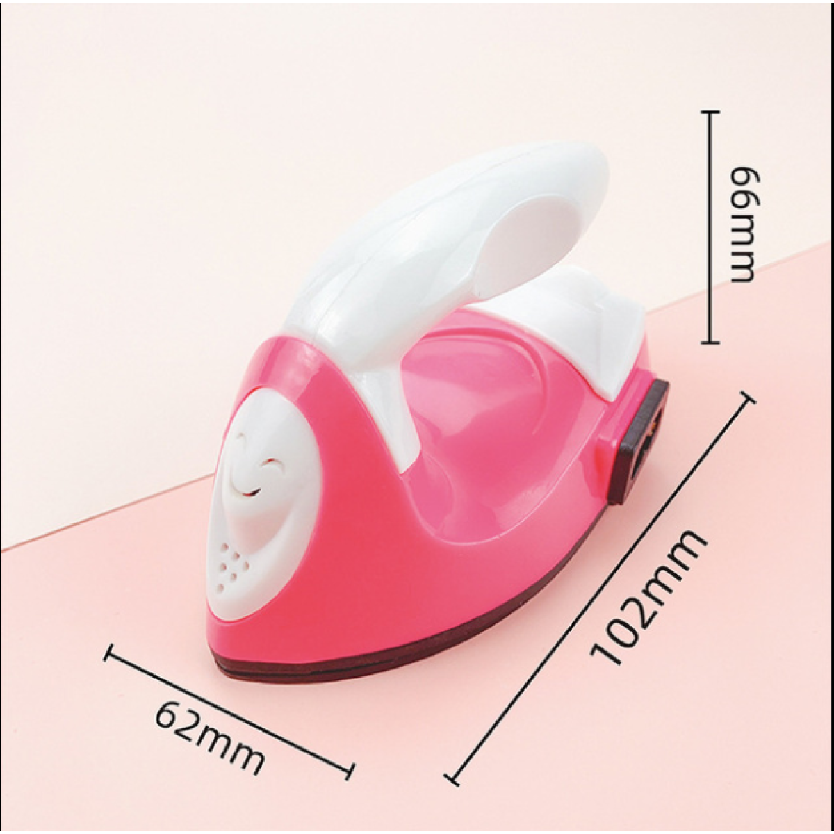 Ein rosa und weißes Spielzeugbügeleisen mit Abmessungen in Millimetern vor hellrosa Hintergrund.